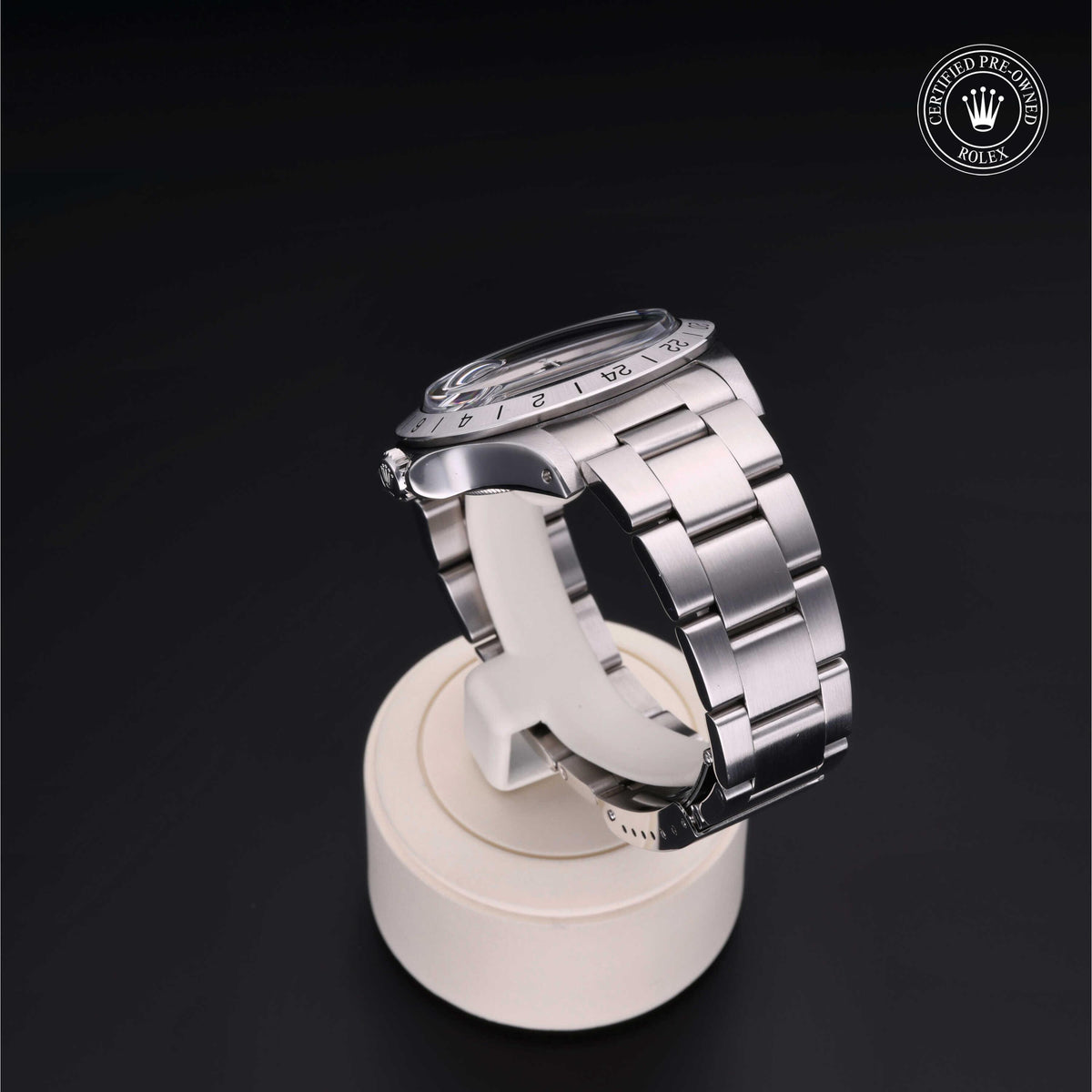 Side view of a silver Rolex watch with a metal link bracelet displayed on a white stand against a black background, featuring a certified pre-owned Rolex logo.