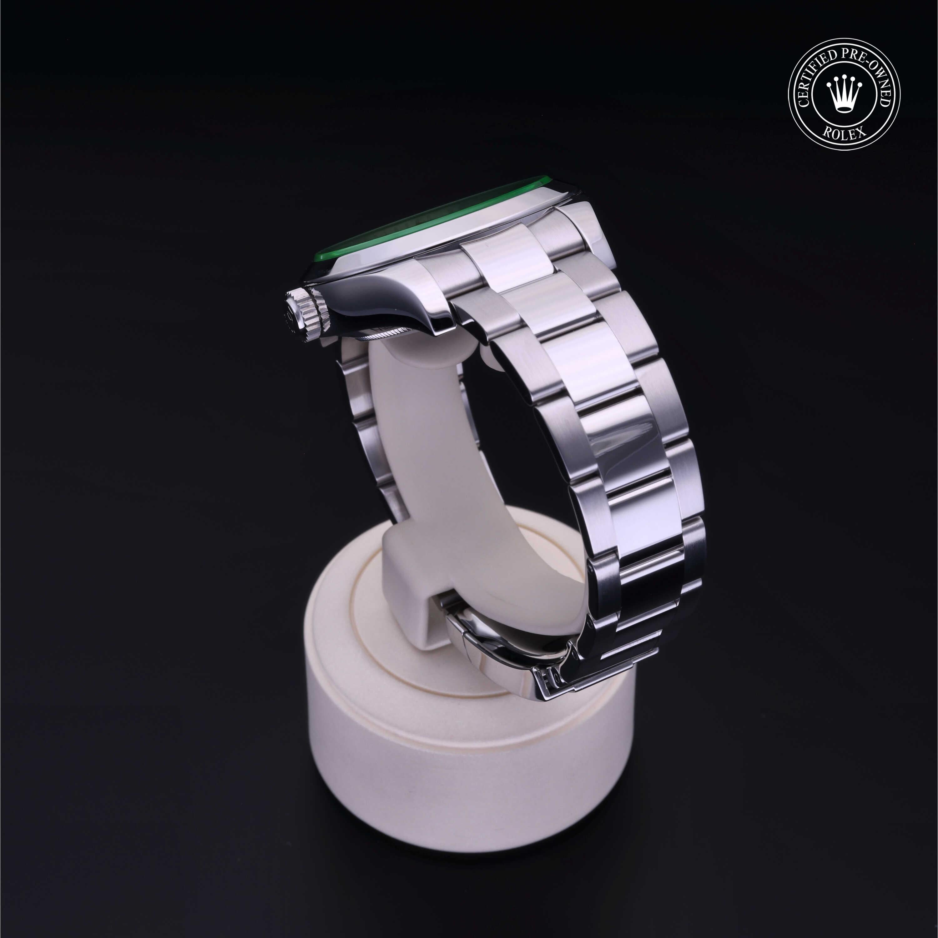 Side view of a luxury stainless steel Rolex watch on a white display stand with a black background, featuring a certified pre-owned Rolex logo in the corner.