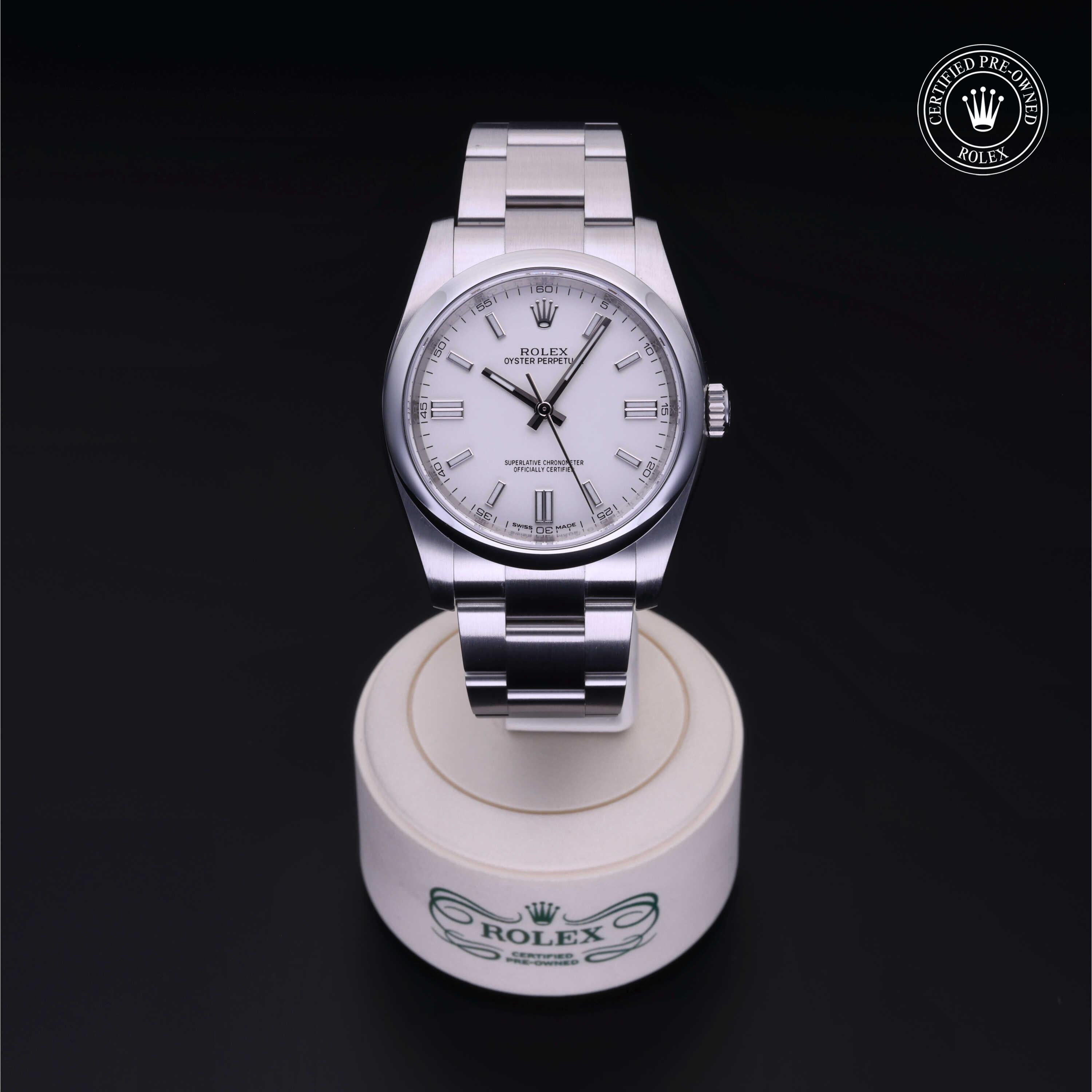 A Rolex stainless steel watch with a white dial displayed on a white circular stand against a black background, featuring a verified pre-owned Rolex emblem in the top corner.