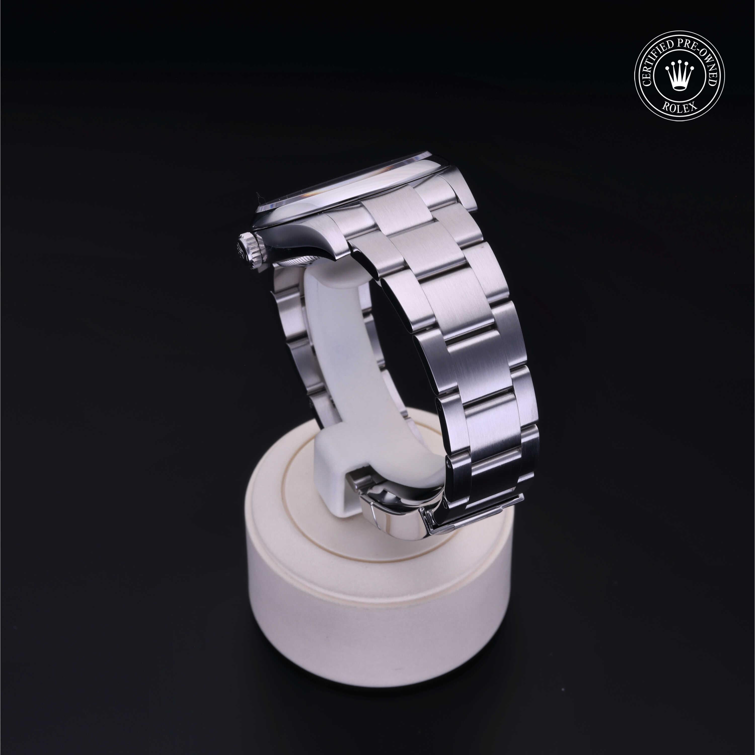 Close-up of a Rolex luxury watch with a polished stainless steel bracelet displayed on a white stand against a black background, featuring a certified pre-owned Rolex emblem.