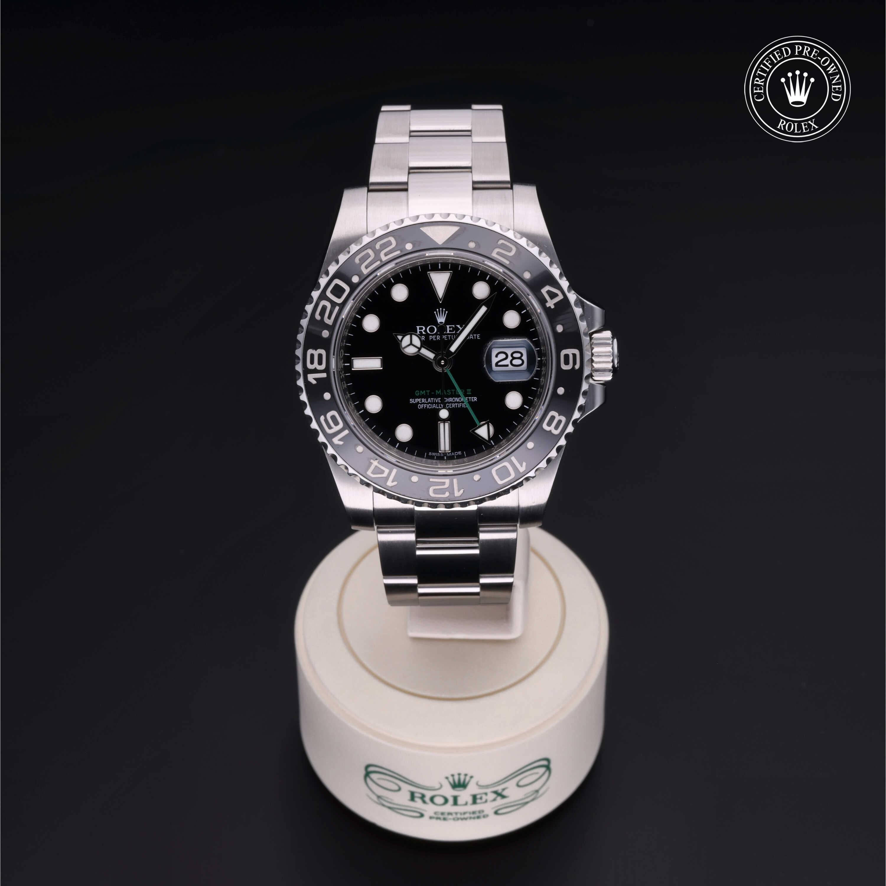 Rolex luxury watch with a black dial and silver bracelet displayed on a branded white stand, featuring a certified pre-owned Rolex logo in the corner.