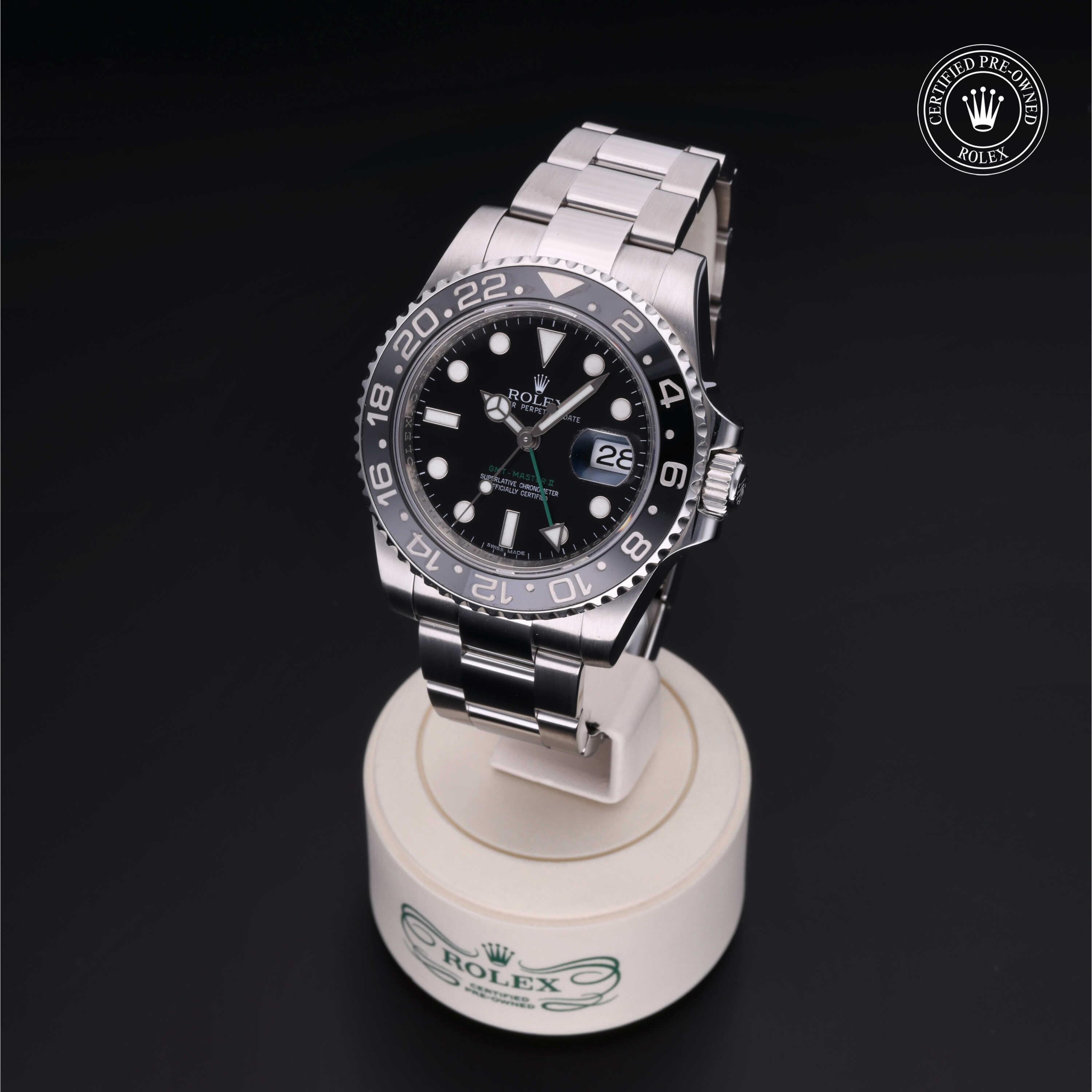 Rolex luxury watch with black dial and silver bezel displayed on a white stand marked with the Rolex logo against a black background, certified pre-owned badge visible.