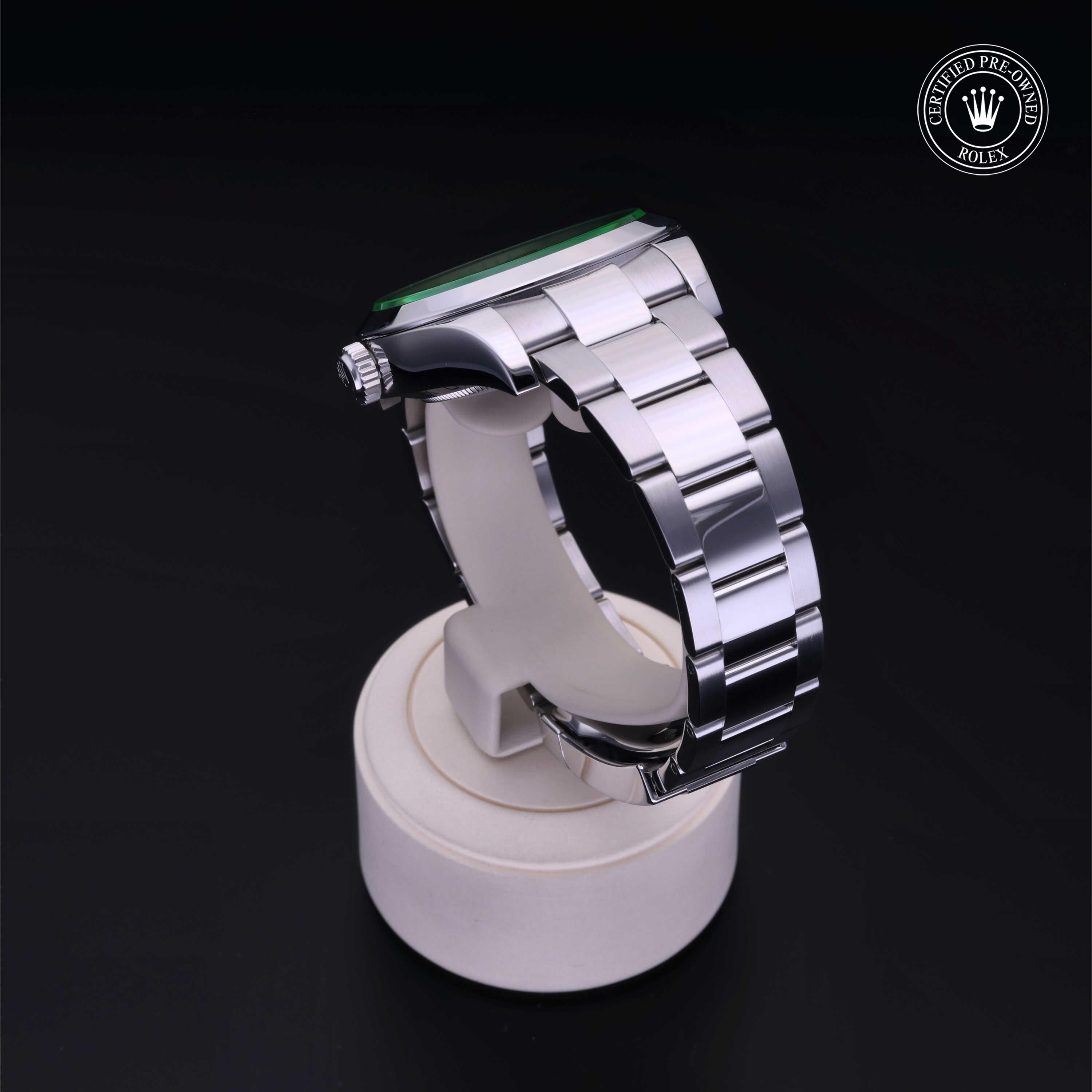 Silver metal watch band with a green bezel displayed on a white circular stand against a black background, featuring a Rolex Certified Pre-Owned logo in the corner.