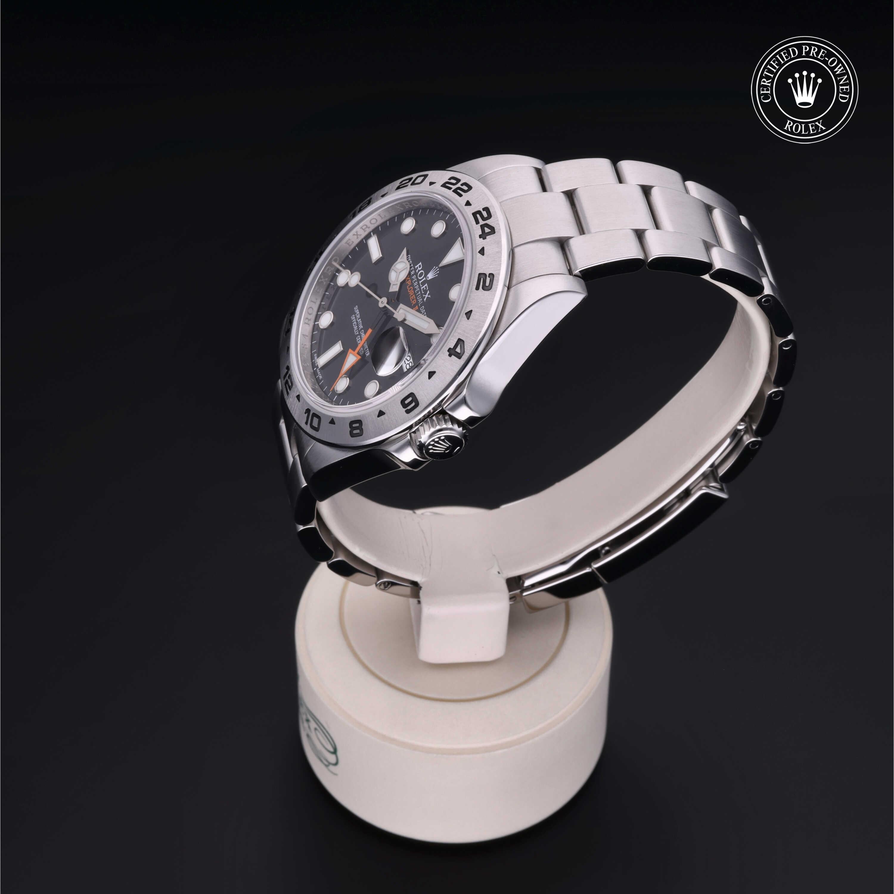 Stainless steel luxury watch with black dial and silver bracelet displayed on a white stand, featuring a Rolex Certified Pre-Owned emblem in the corner.