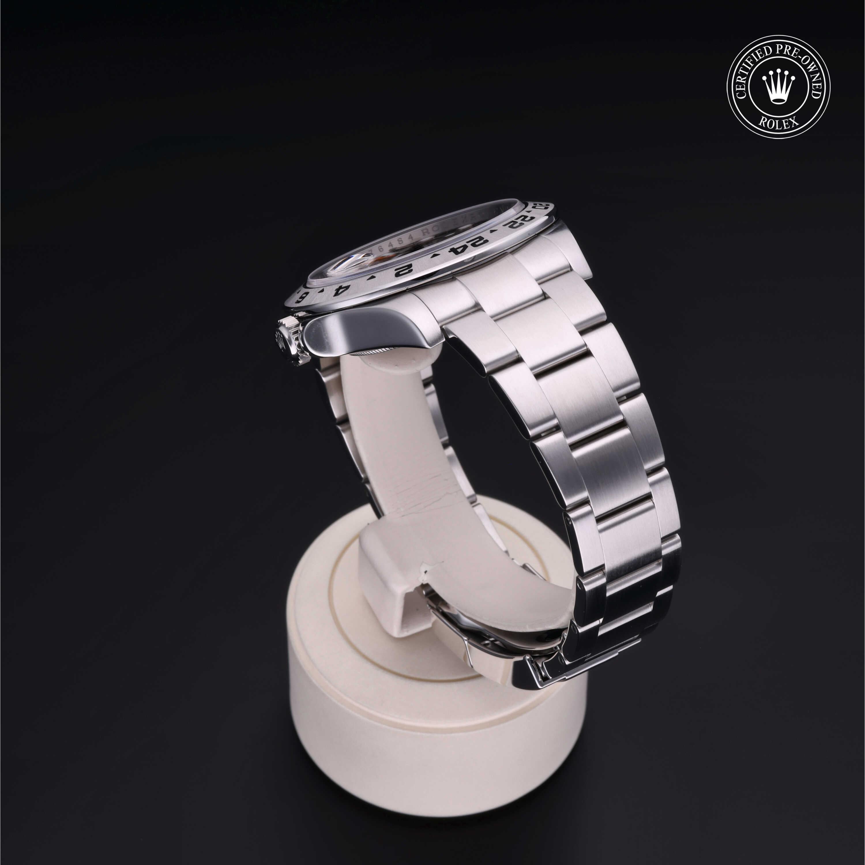 Side view of a luxury stainless steel Rolex watch displayed on a white stand against a dark background with a certified pre-owned Rolex logo in the corner.
