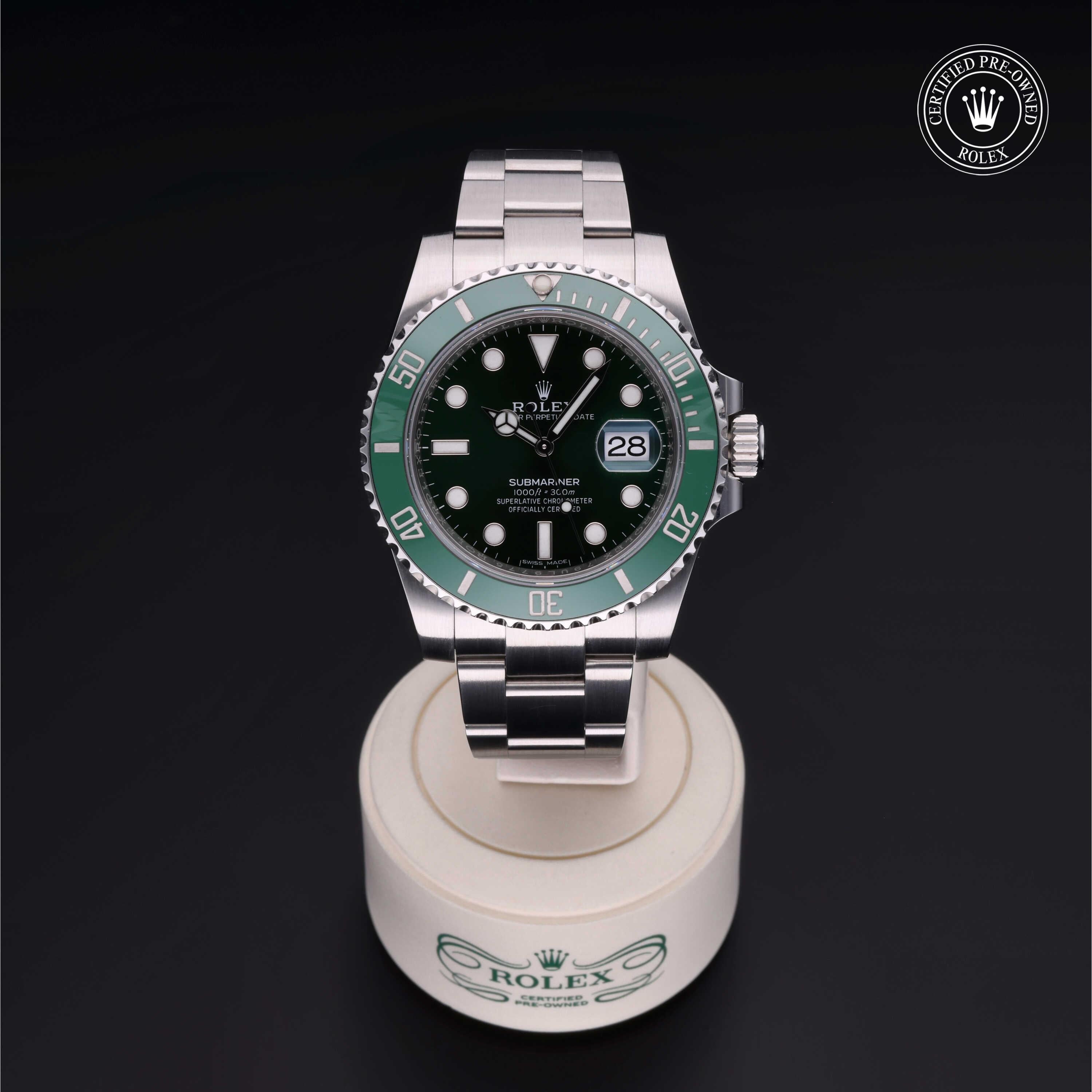 Silver Rolex Submariner watch with green bezel and black dial displayed on a white stand against a black background, featuring a certified pre-owned Rolex logo badge.