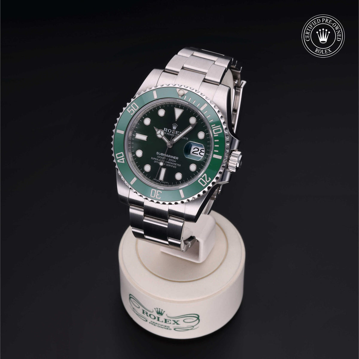 Rolex Submariner wristwatch with green bezel and black dial displayed on a branded stand, featuring Rolex Certified Pre-Owned logo on a dark background.