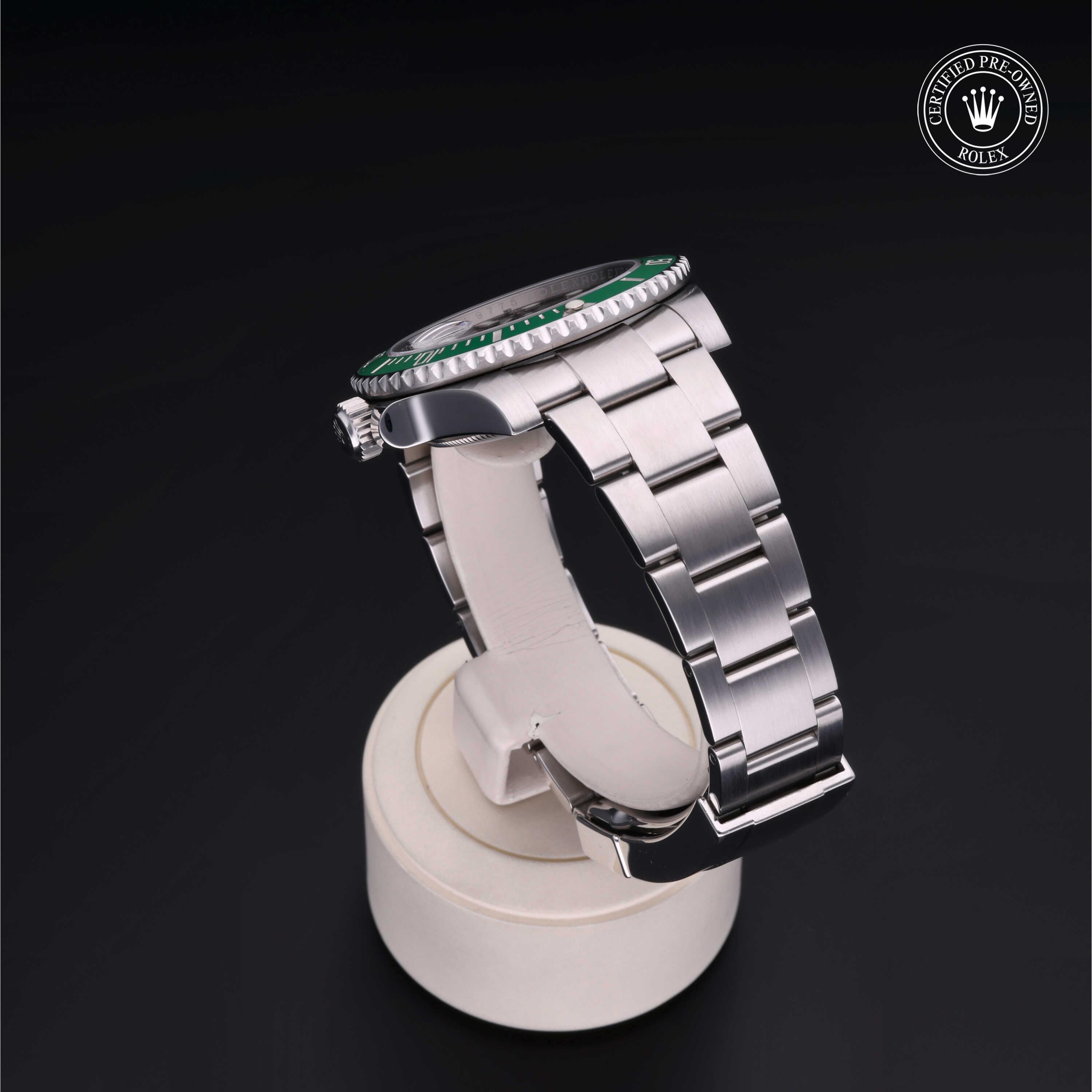 Side view of a stainless steel Rolex wristwatch with a green bezel displayed on a white stand, featuring a stainless steel bracelet and a certified pre-owned Rolex logo in the corner.