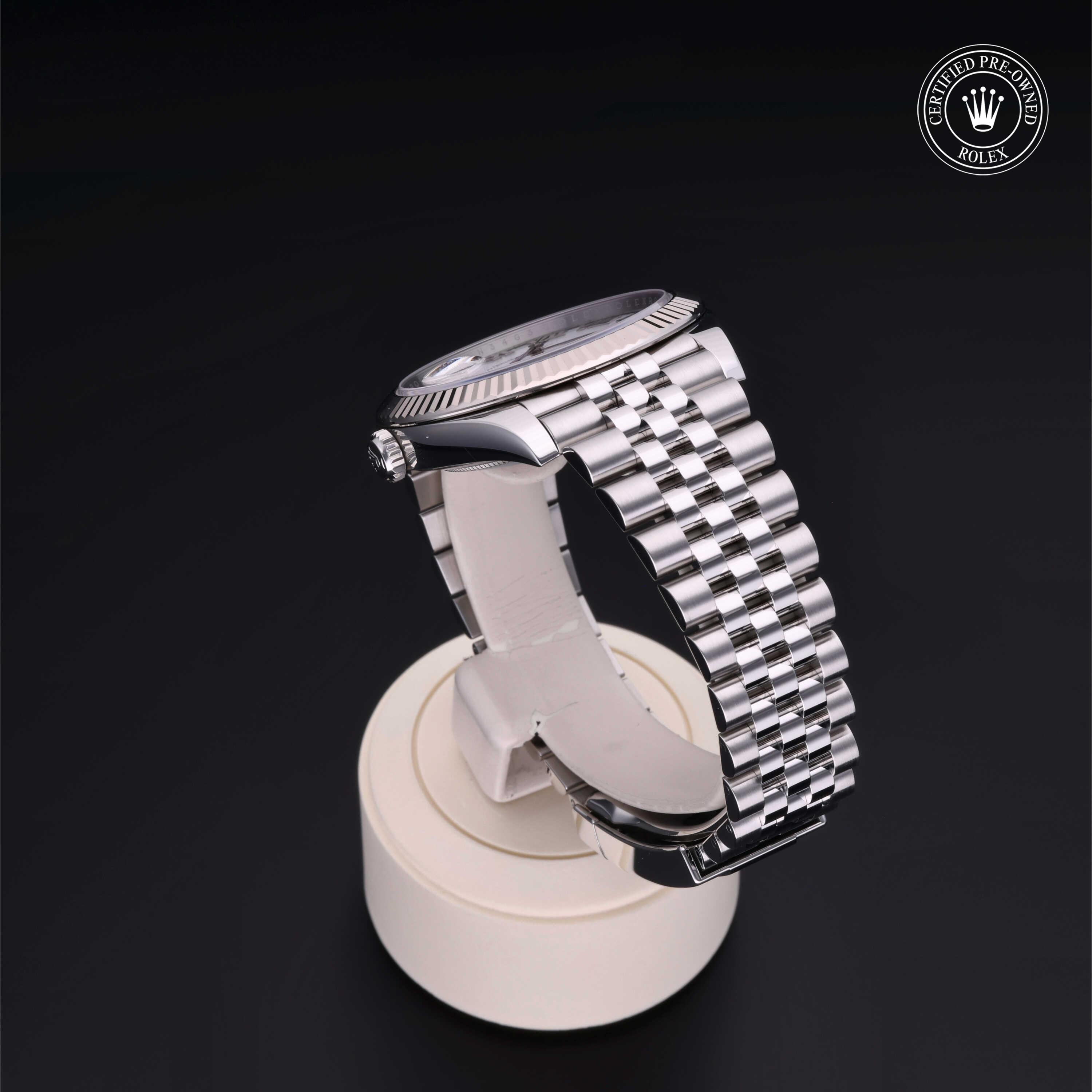 Silver Rolex watch with a polished metal link bracelet displayed on a white stand against a black background, featuring a certified pre-owned Rolex logo.