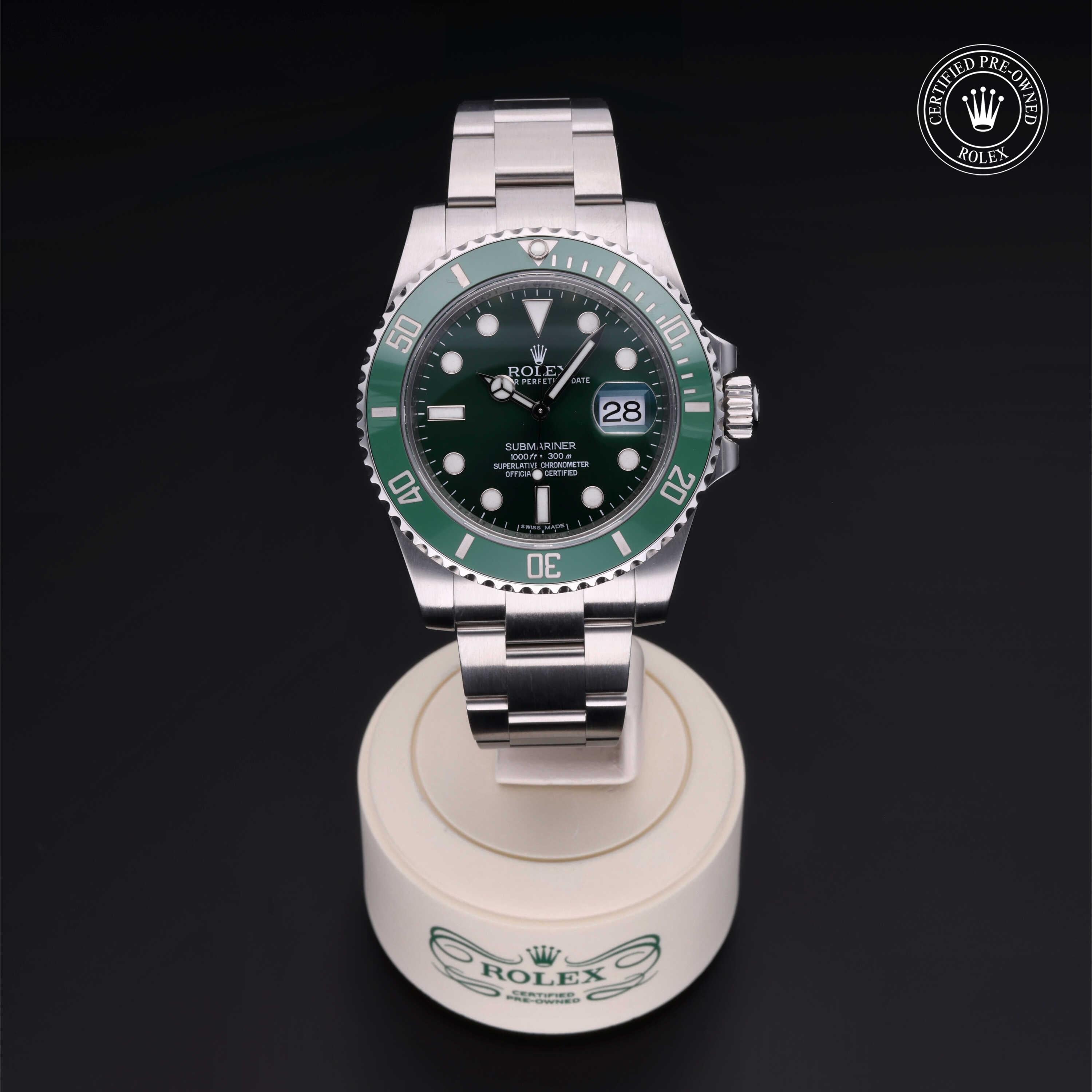 Rolex Submariner luxury watch with green bezel and black dial displayed on a white stand, featuring a stainless steel bracelet and certified pre-owned badge.