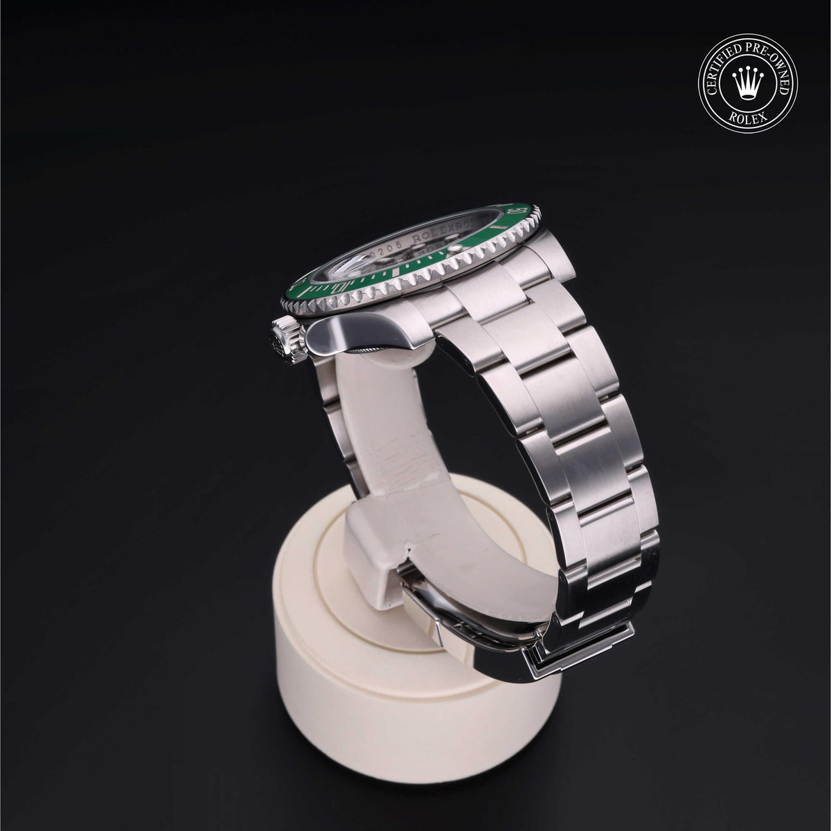 Rolex luxury watch with a silver metal bracelet and green bezel displayed on a white stand against a black background, featuring a Rolex Certified Pre-Owned logo.