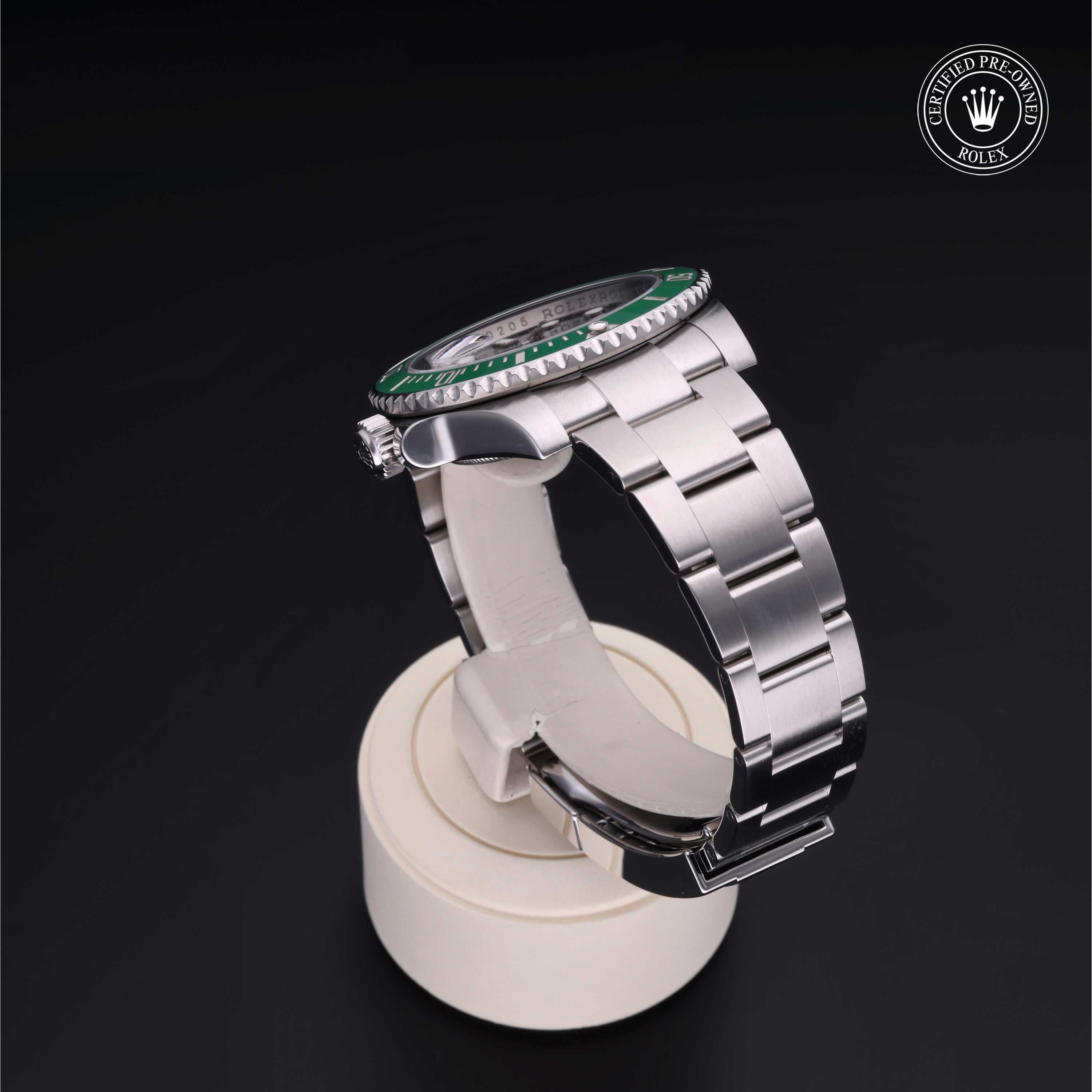 Rolex luxury watch with a silver metal bracelet and green bezel displayed on a white stand against a black background, featuring a Rolex Certified Pre-Owned logo.