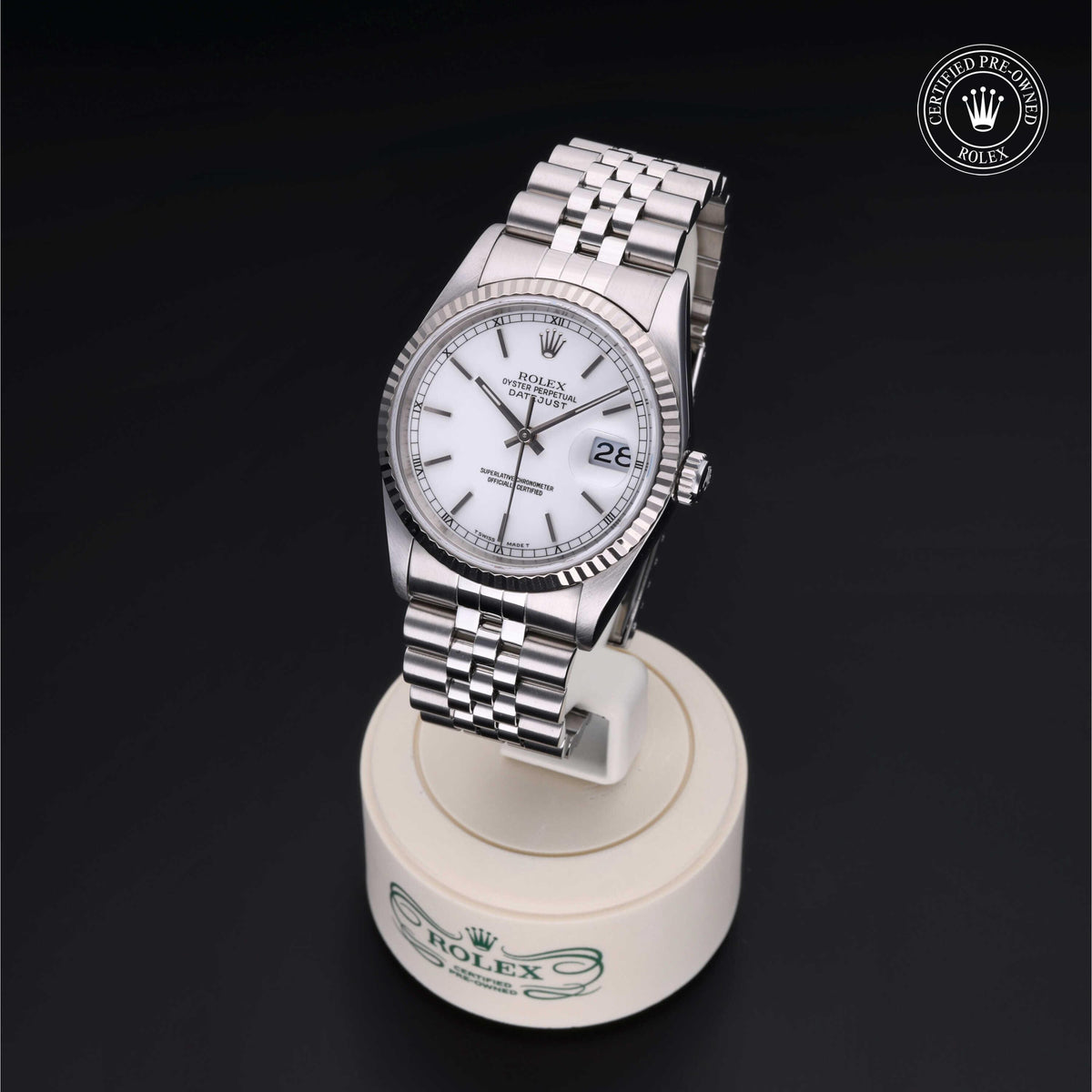 Silver Rolex wristwatch with white dial, date display, and fluted bezel resting on a branded round stand against a black background, featuring a Certified Pre-Owned Rolex logo.