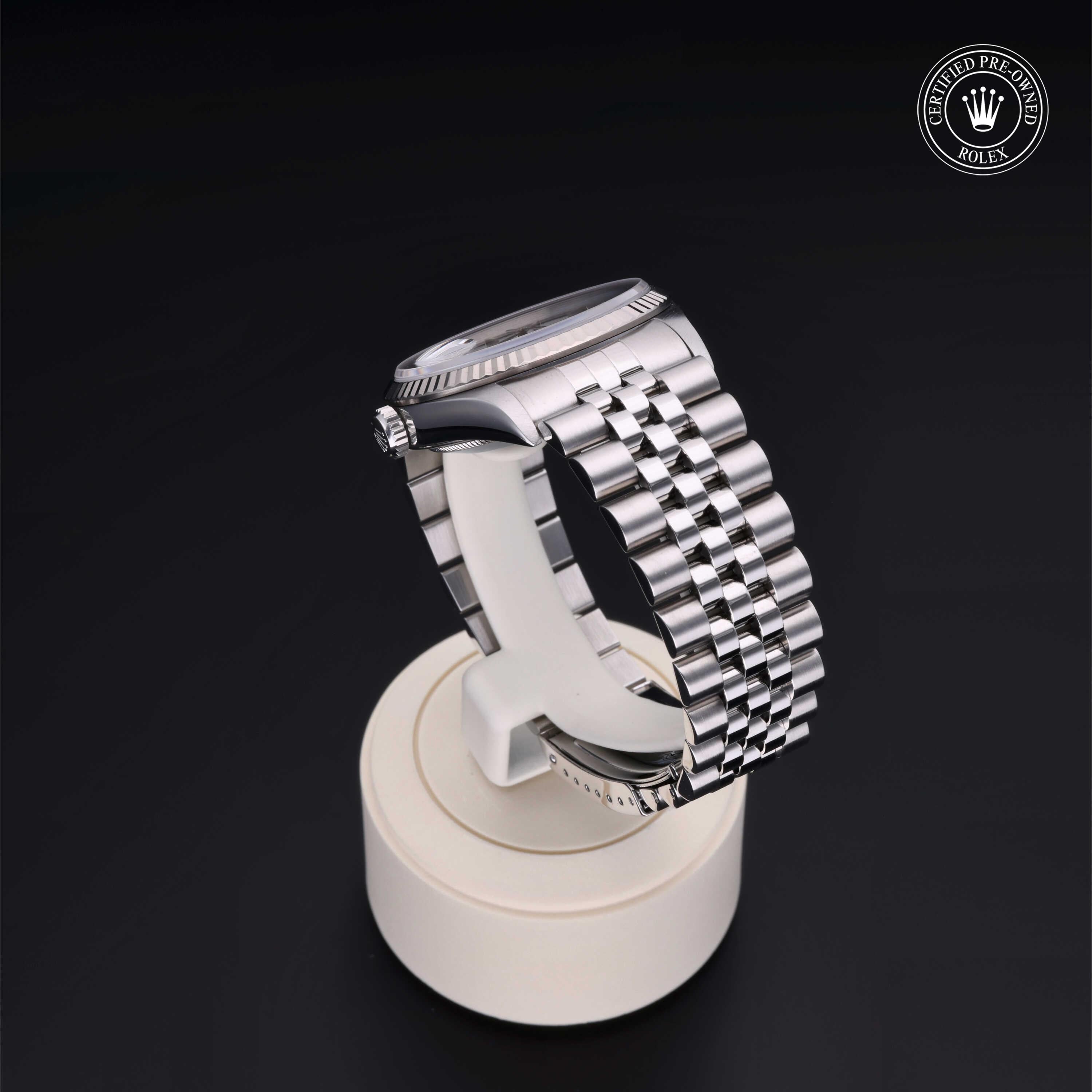Silver luxury watch with a polished metal link bracelet displayed on a white stand against a black background, featuring a certified pre-owned Rolex logo in the corner.