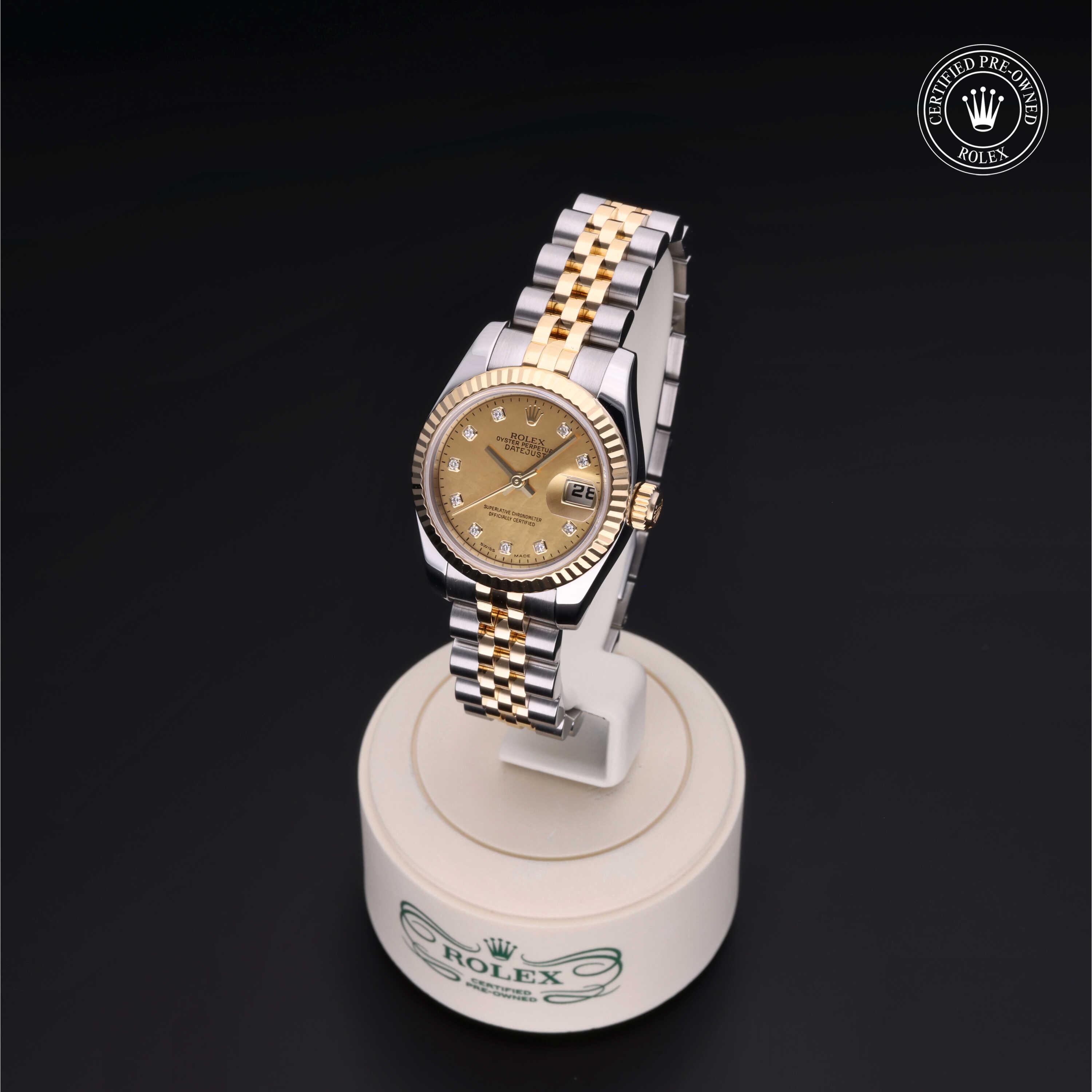 Two-tone Rolex wristwatch with gold dial and diamond hour markers displayed on a white Rolex-branded stand against a black background, showcasing luxury and craftsmanship.