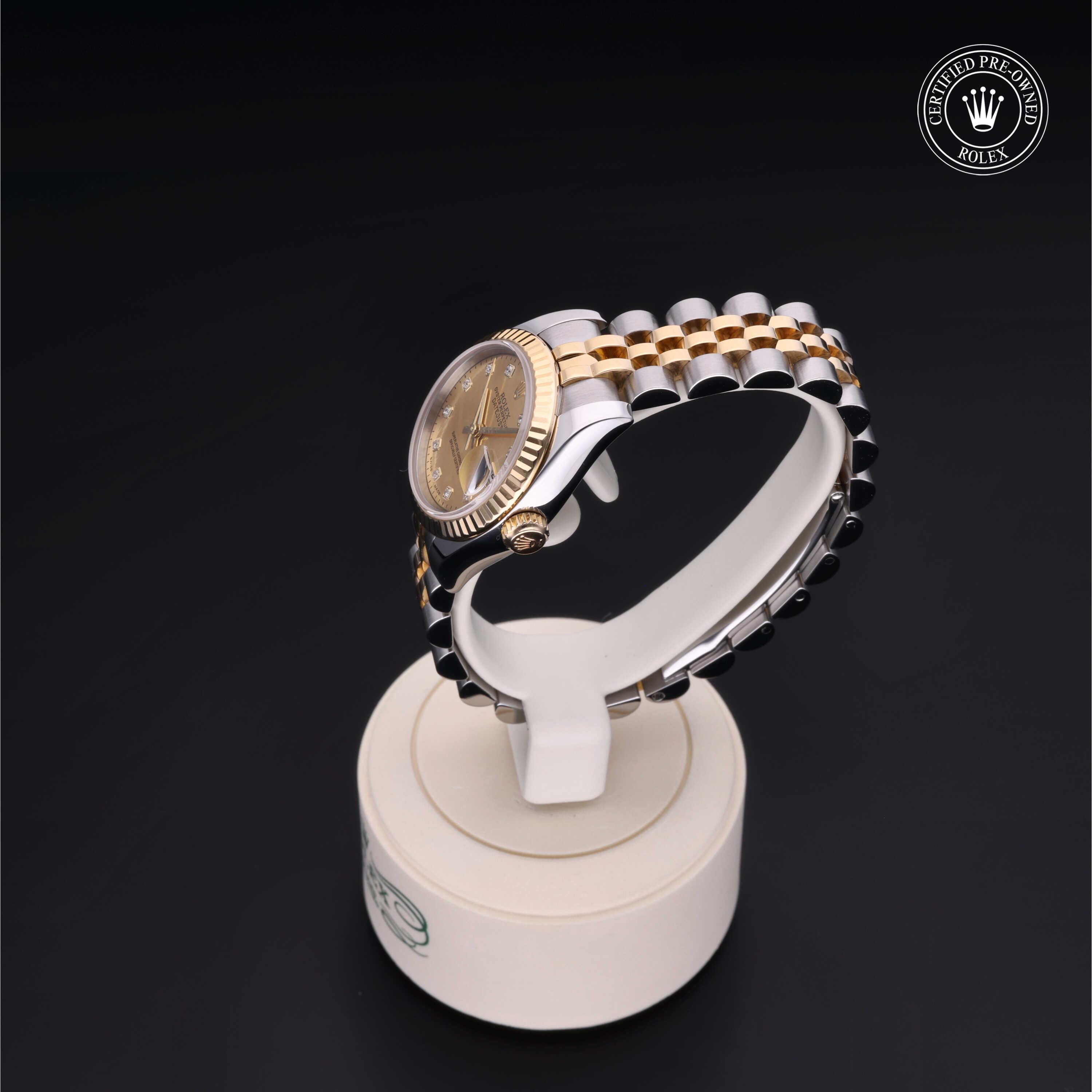 Two-tone luxury watch with gold and silver links on a round display stand against a black background, featuring a certified pre-owned Rolex emblem.