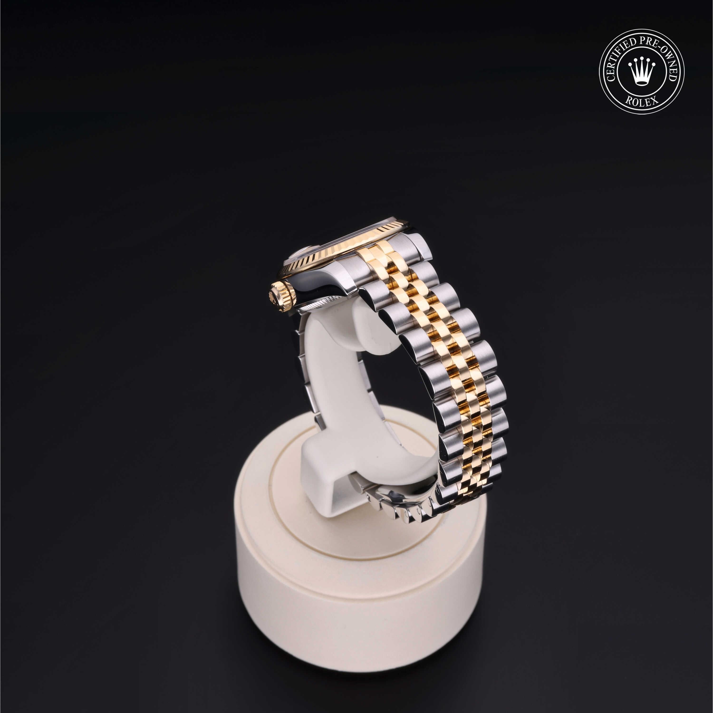 A Rolex luxury watch band in silver and gold tones displayed on a white stand against a black background, featuring a certified pre-owned Rolex logo.