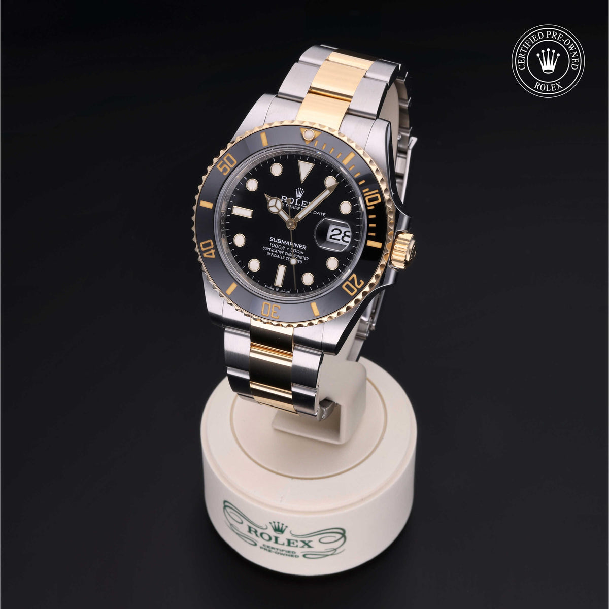 Rolex two-tone luxury watch with black dial and gold accents displayed on a stand, featuring date window and certified pre-owned Rolex logo.