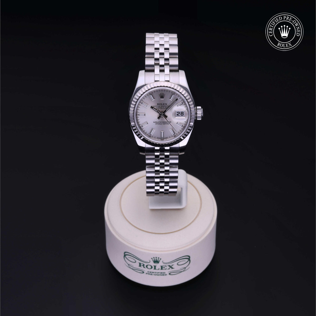 Silver Rolex watch with a white dial and date display on a white pedestal against a black background, featuring the Rolex Certified Pre-Owned logo.