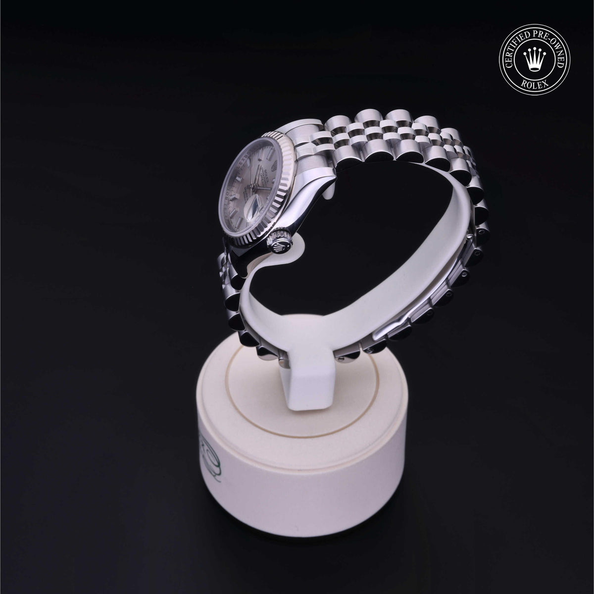 Luxury silver Rolex watch with a polished metal link bracelet displayed on a white stand against a black background, featuring a 