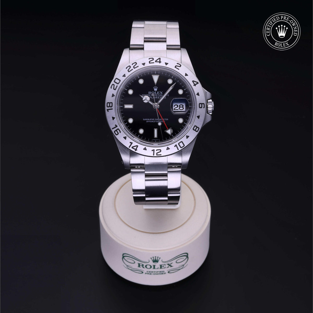 Close-up of a stainless steel Rolex watch with black dial and date display, standing on a branded round white stand against a black background, featuring a Certified Pre-Owned Rolex logo.