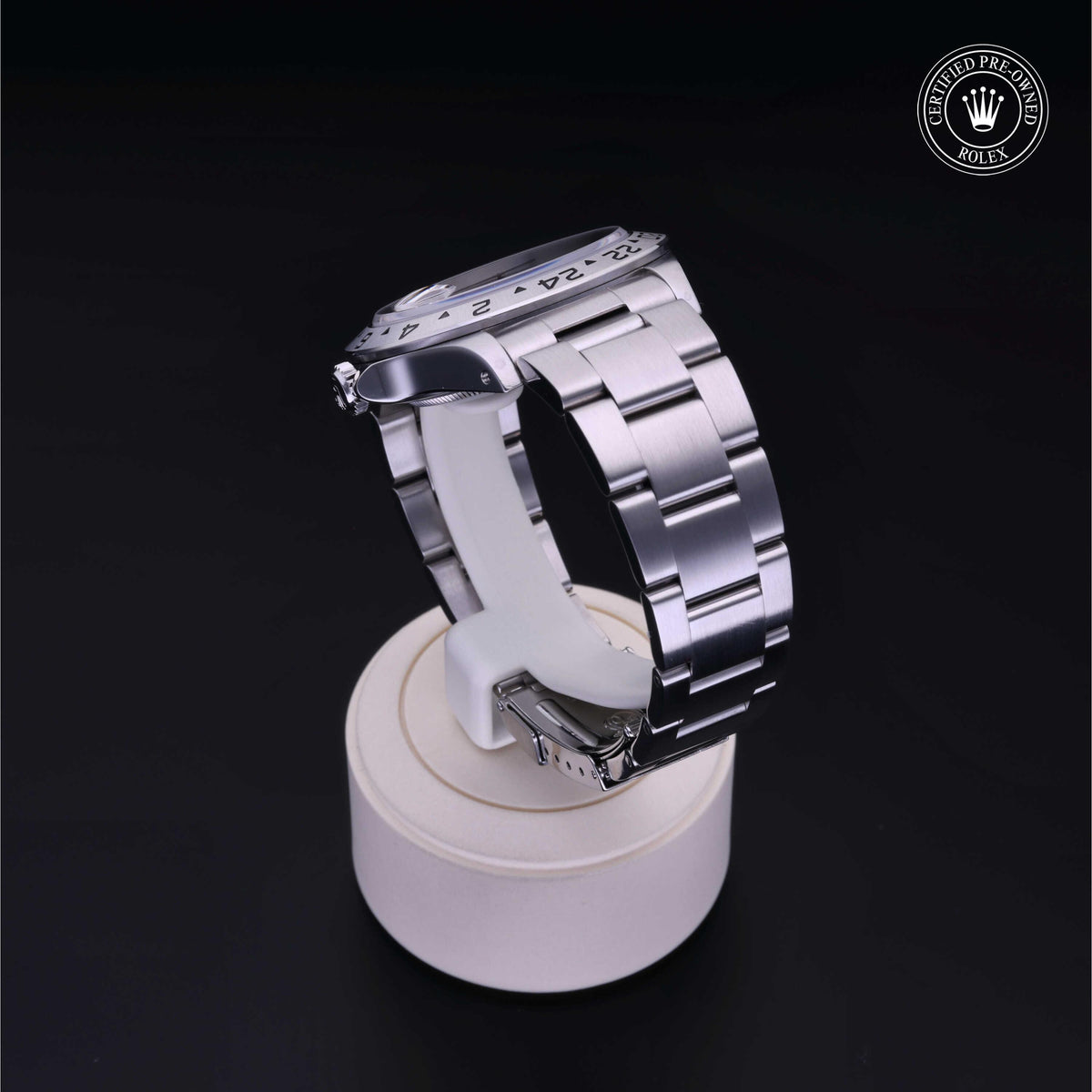 Silver Rolex luxury watch with a stainless steel bracelet displayed on a white circular stand against a black background, featuring a certified pre-owned Rolex logo.