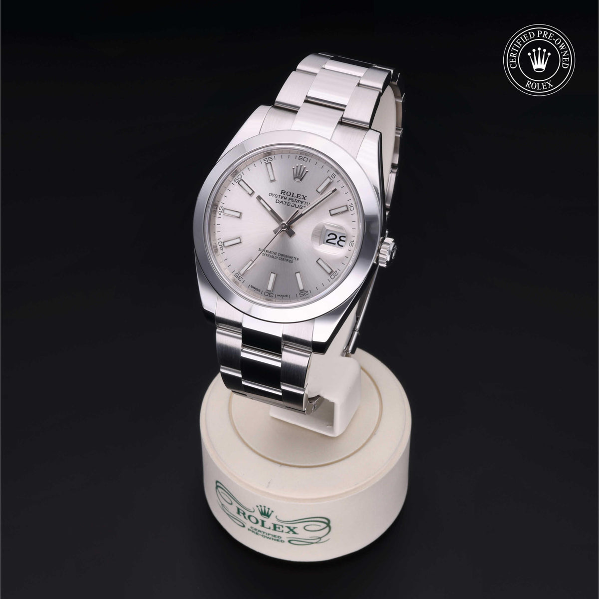 Silver Rolex wristwatch with a stainless steel band displayed on a white stand with the Rolex logo, featuring a date window and 