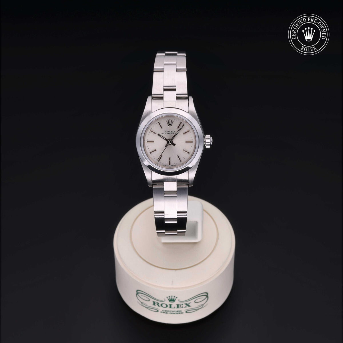 Silver Rolex wristwatch with a white face and stainless steel band displayed on a round white stand with the Rolex logo, set against a black background.