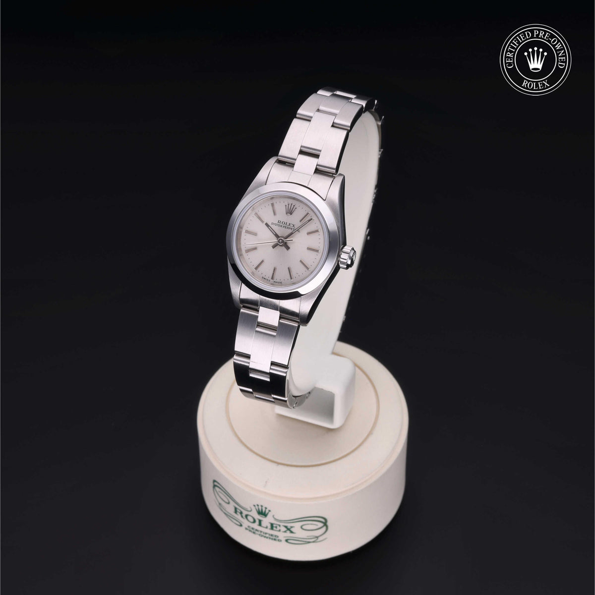 Silver Rolex wristwatch with a classic white dial displayed on a round white stand, featuring the Rolex Certified Pre-Owned logo in the corner.