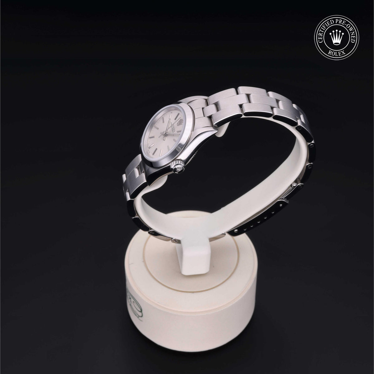 Silver stainless steel Rolex watch with a smooth bezel and classic dial displayed on a white stand against a black background with a certified pre-owned Rolex emblem.