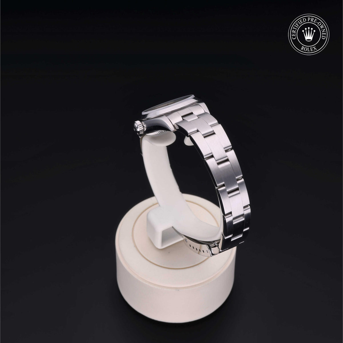 Side view of a stainless steel luxury watch with a metal link bracelet on a white display stand, featuring a certified pre-owned Rolex logo.