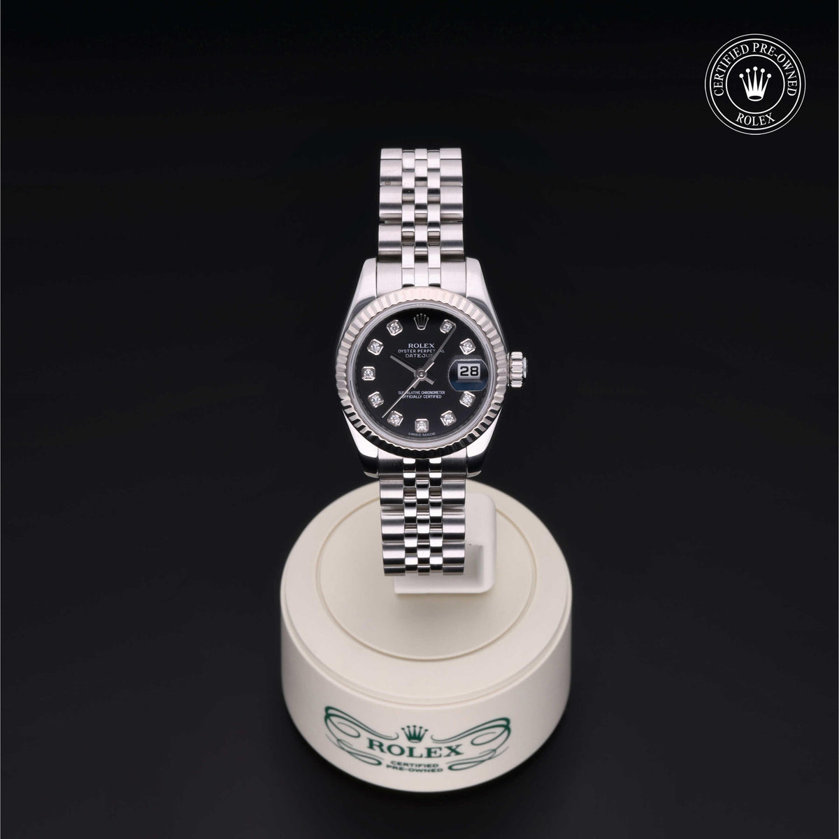 Rolex luxury watch with a black dial and diamond hour markers on a silver jubilee bracelet, displayed on a white Rolex stand with a certified pre-owned logo above.