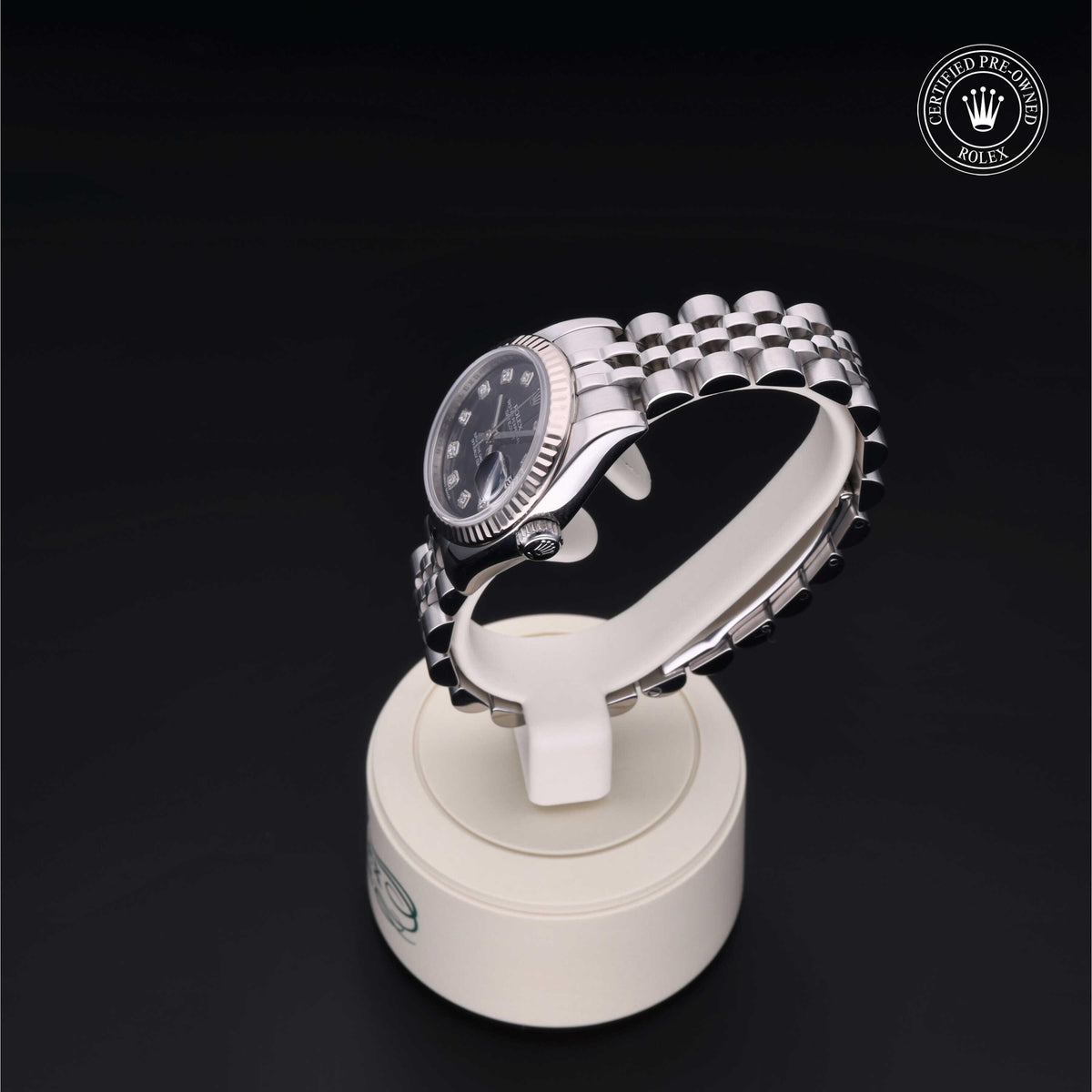 Luxury Rolex watch with a stainless steel jubilee bracelet displayed on a white stand against a black background, featuring a certified pre-owned emblem.