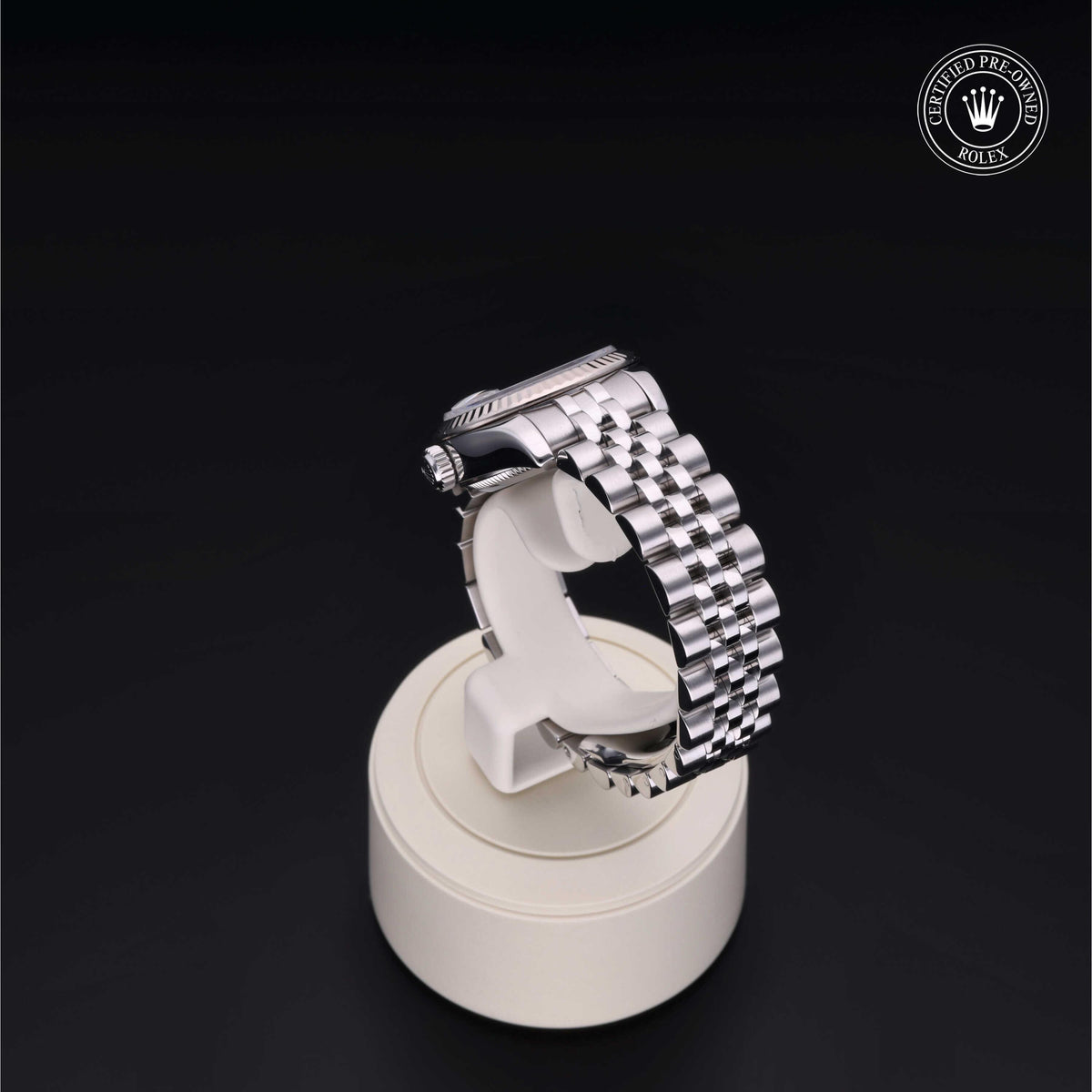 Side view of a luxury silver metal Rolex watch band displayed on a white stand with a Certified Pre-Owned Rolex logo in the corner on a black background