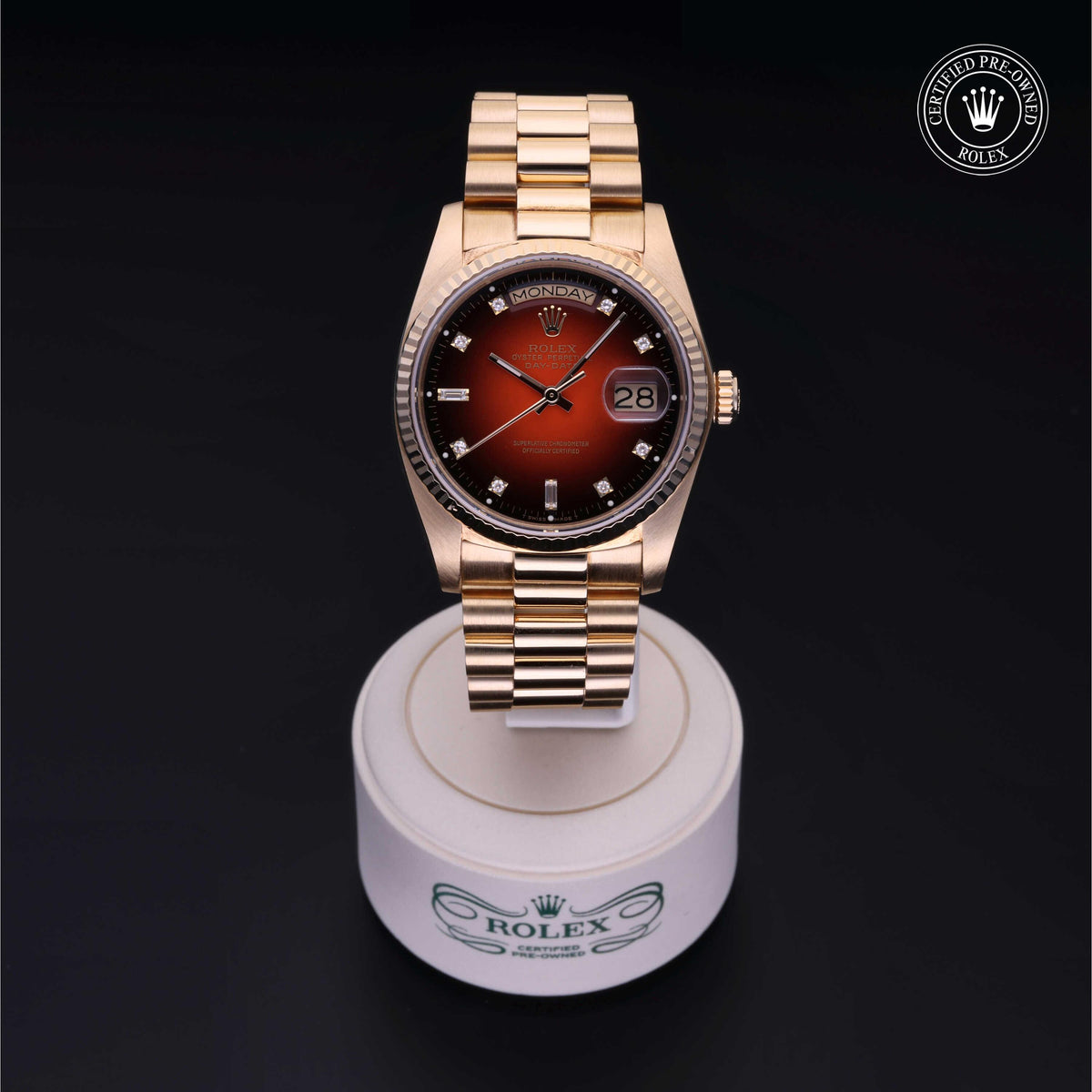 Gold Rolex luxury watch with red gradient dial, diamond hour markers, and date display, shown on a white branded stand with certified pre-owned logo.