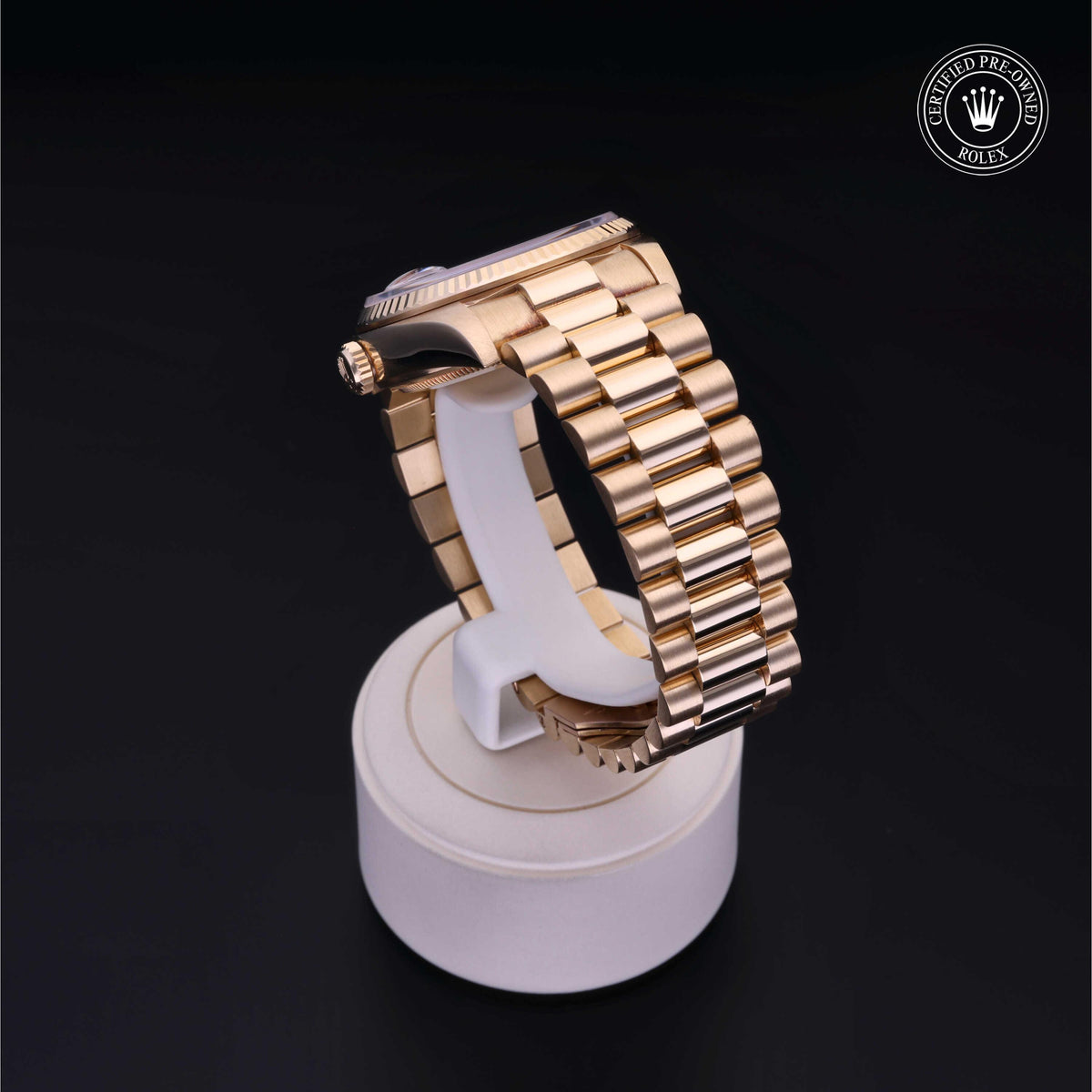 Side view of a gold luxury watch with a polished metal bracelet displayed on a white stand against a black background with a Rolex Certified Pre-Owned logo in the corner.
