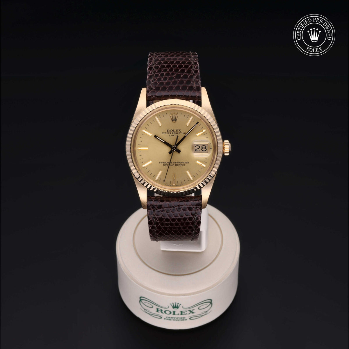 Gold Rolex wristwatch with brown leather strap displayed on a round white stand, featuring a date window and Rolex Certified Pre-Owned logo in the corner.