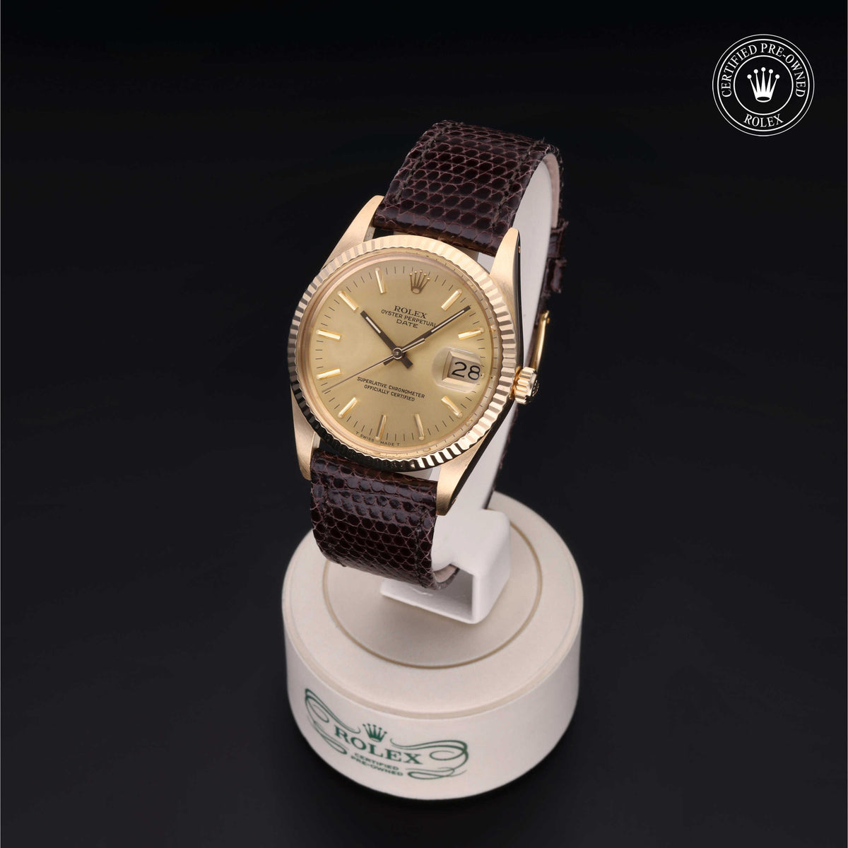 Gold Rolex watch with fluted bezel and brown leather strap displayed on a white stand with Rolex logo, featuring a date window and certified pre-owned badge.