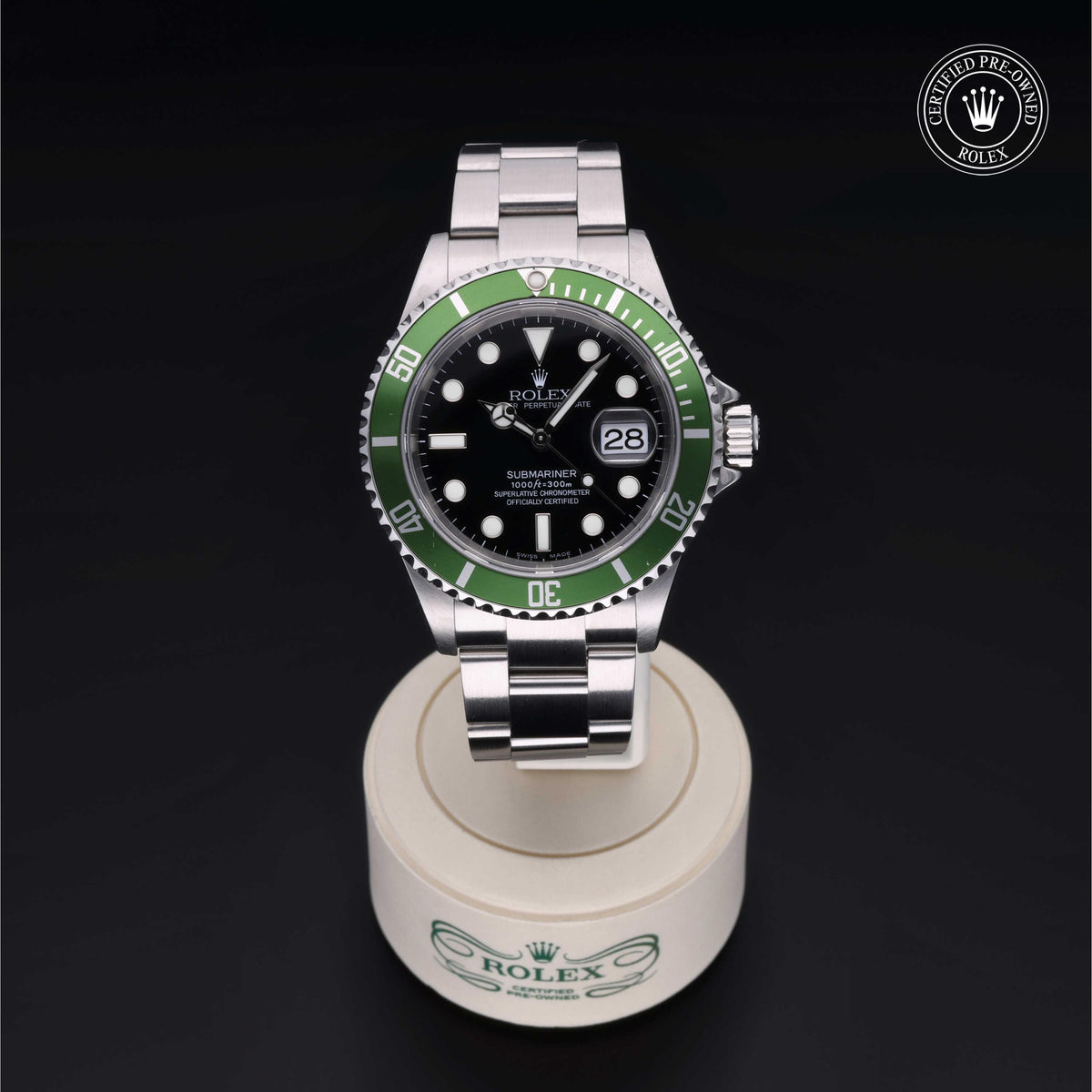 Rolex Submariner watch with a green bezel and black dial on a stainless steel bracelet, displayed on a branded stand against a black background, certified pre-owned.