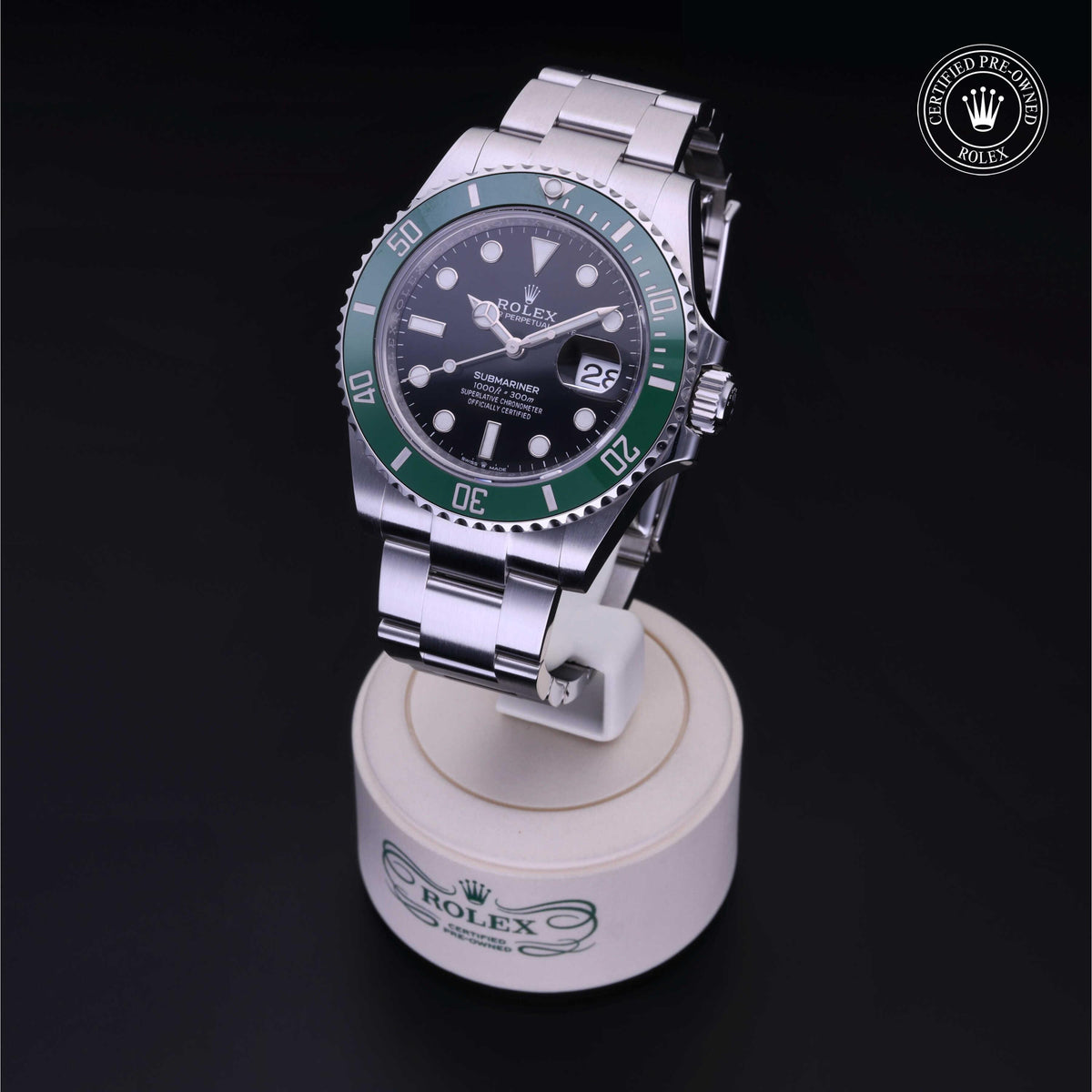 Silver Rolex Submariner watch with green bezel and black dial displayed on a white stand with Rolex branding, accompanied by a certified pre-owned Rolex logo on a black background.