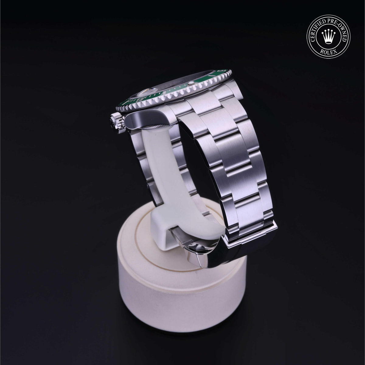 Side view of a stainless steel Rolex watch with a metal link bracelet displayed on a white stand, featuring a Rolex Certified Pre-Owned logo on a black background.