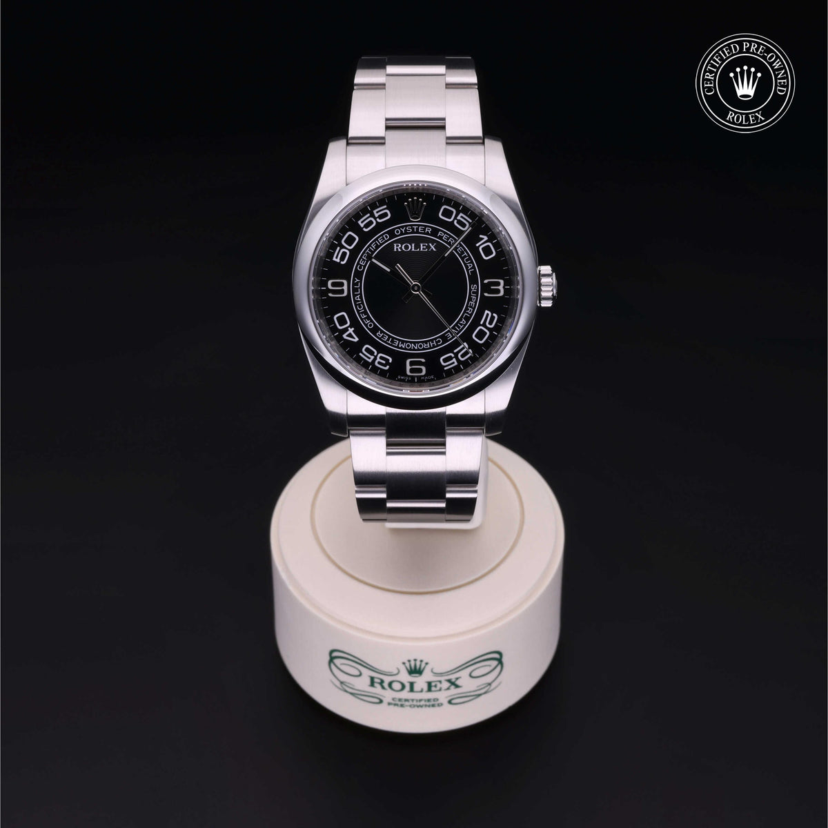Silver Rolex luxury watch with black dial and Arabic numerals on a white display stand against a black background, featuring a 