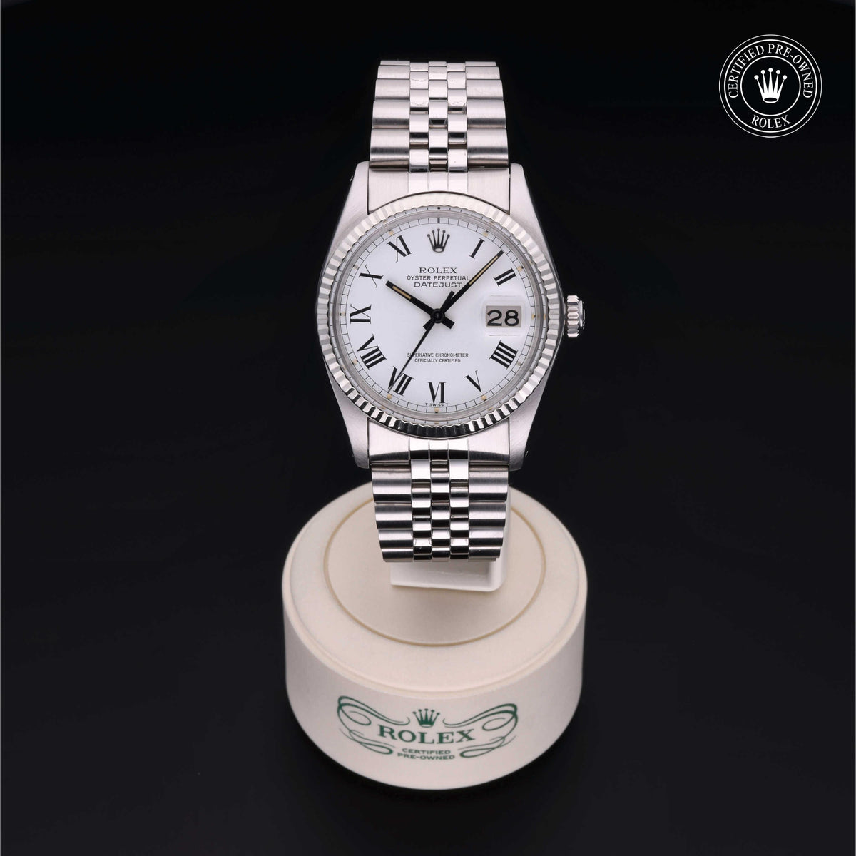 Silver Rolex Oyster Perpetual Datejust watch with white dial, Roman numerals, date display, and jubilee bracelet displayed on a branded stand with a certified pre-owned Rolex logo.