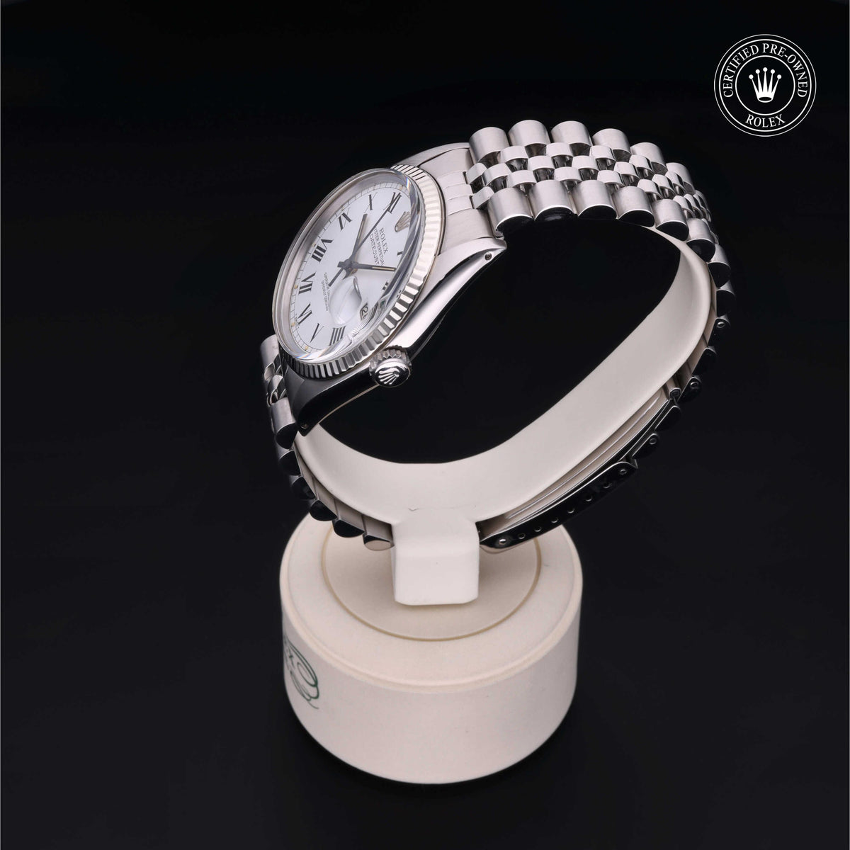 Silver-tone Rolex wristwatch with white dial and Roman numerals on a metal link bracelet, displayed on a white stand against a black background, featuring a Certified Pre-Owned Rolex logo.
