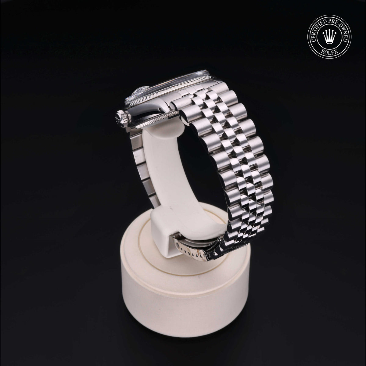 Silver stainless steel Rolex watch with a polished link bracelet displayed on a white round stand against a black background, featuring a Rolex Certified Pre-Owned logo.