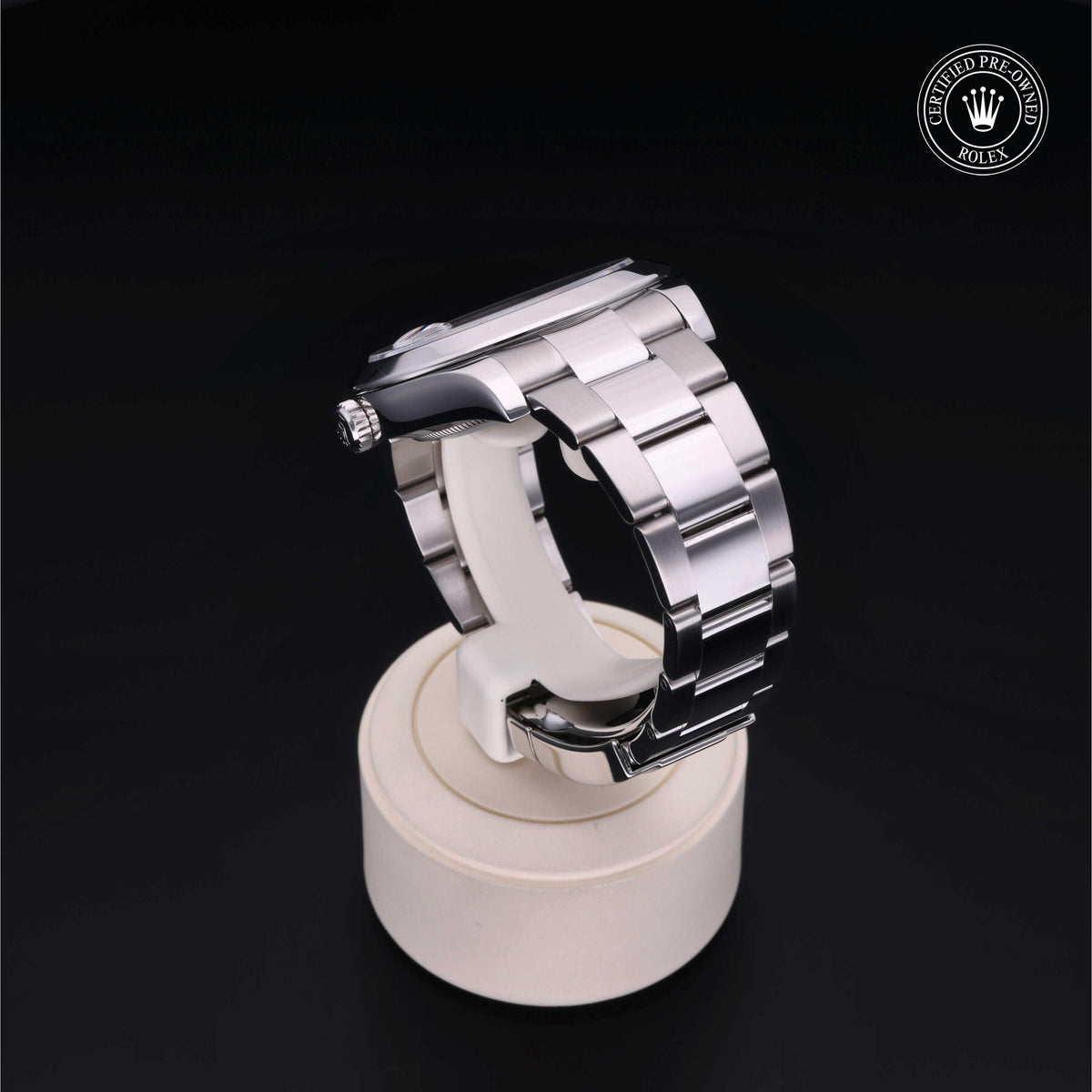 Close-up of a polished stainless steel luxury watch band displayed on a white stand against a black background, featuring a certified pre-owned Rolex logo.