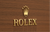 Gold Rolex Logo on Warm Tone Wood Grain Wall